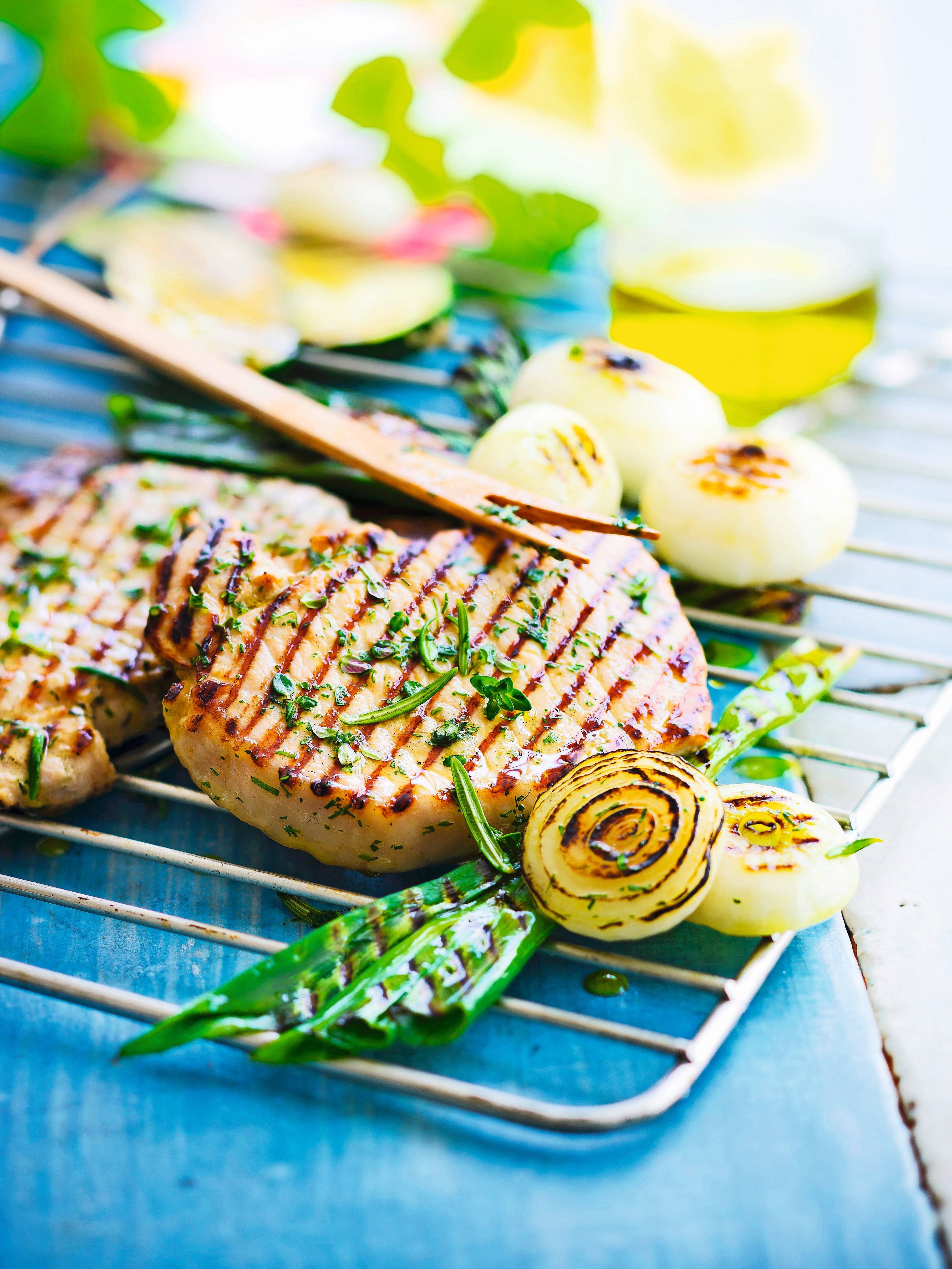Gegrillte Thunfischsteaks mit Kräutern, Zwiebeln und grünen Bohnen auf einem Grillrost.
