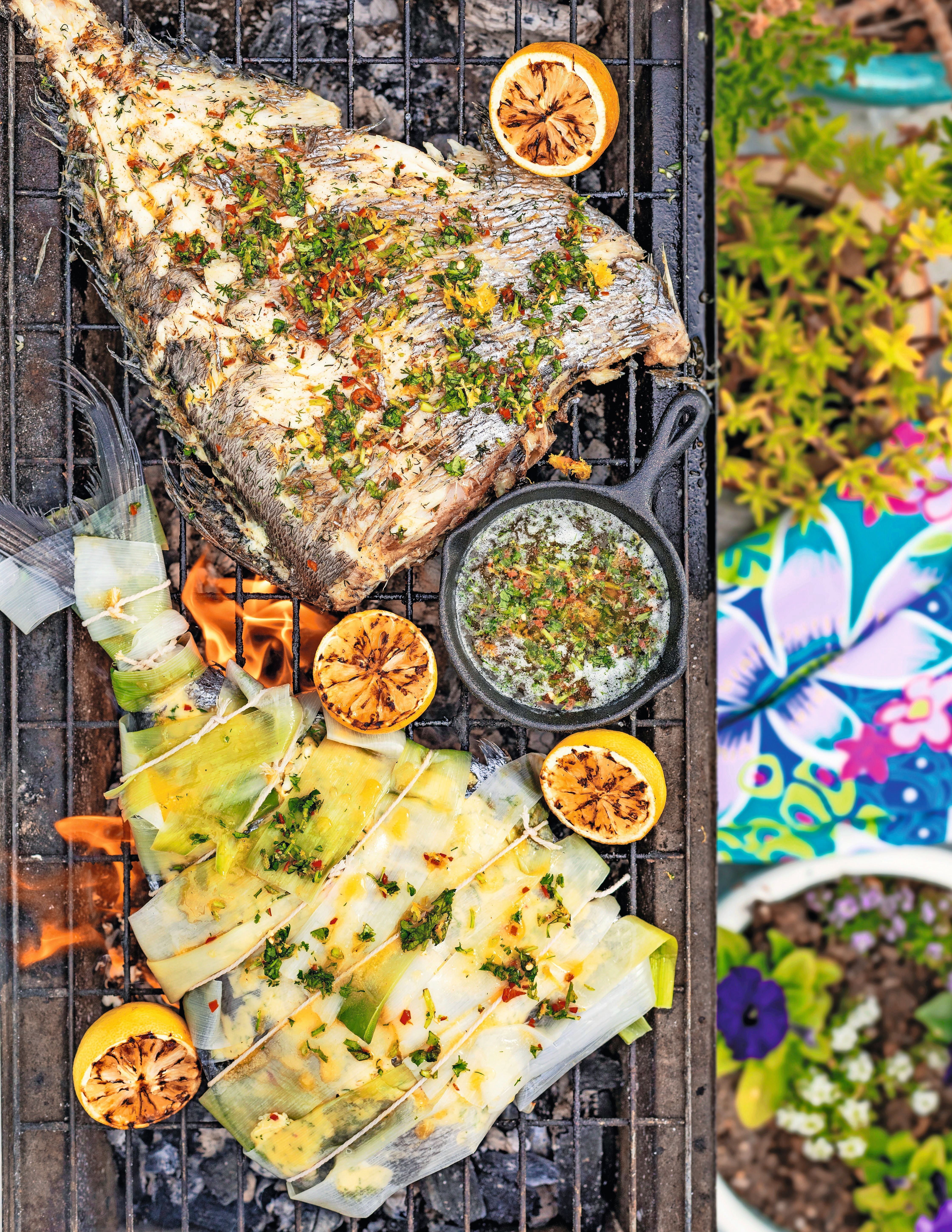 Gegrillter Fisch im Lauchmantel mit Kräutern, dazu halbierte Limetten und Kräuterbutter auf dem Grill.