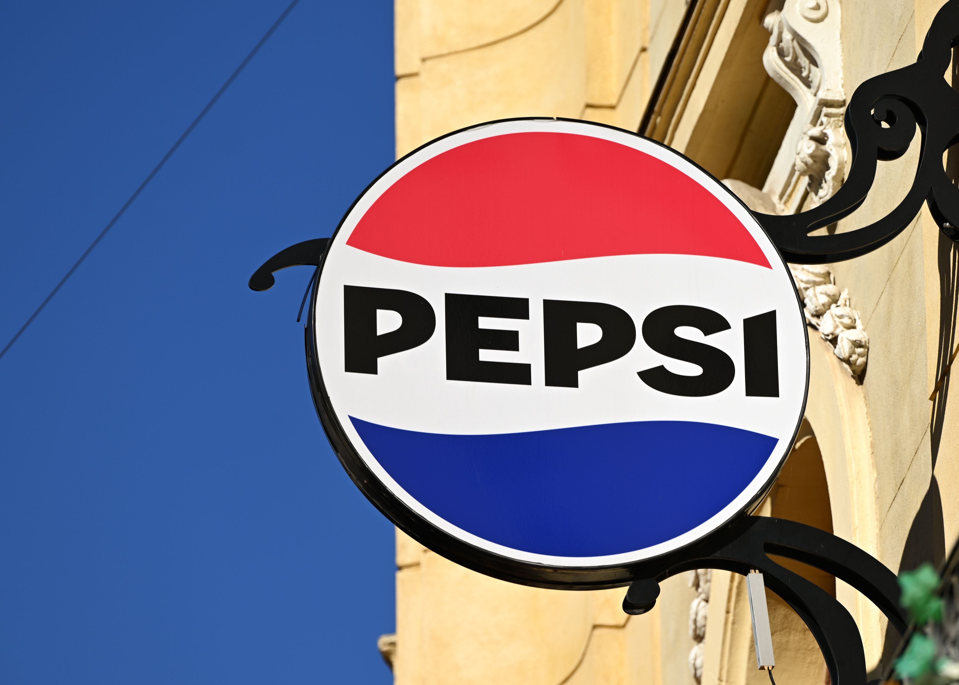Pepsi-Logo als Werbeschild an einer Gebäudewand bei blauem Himmel.