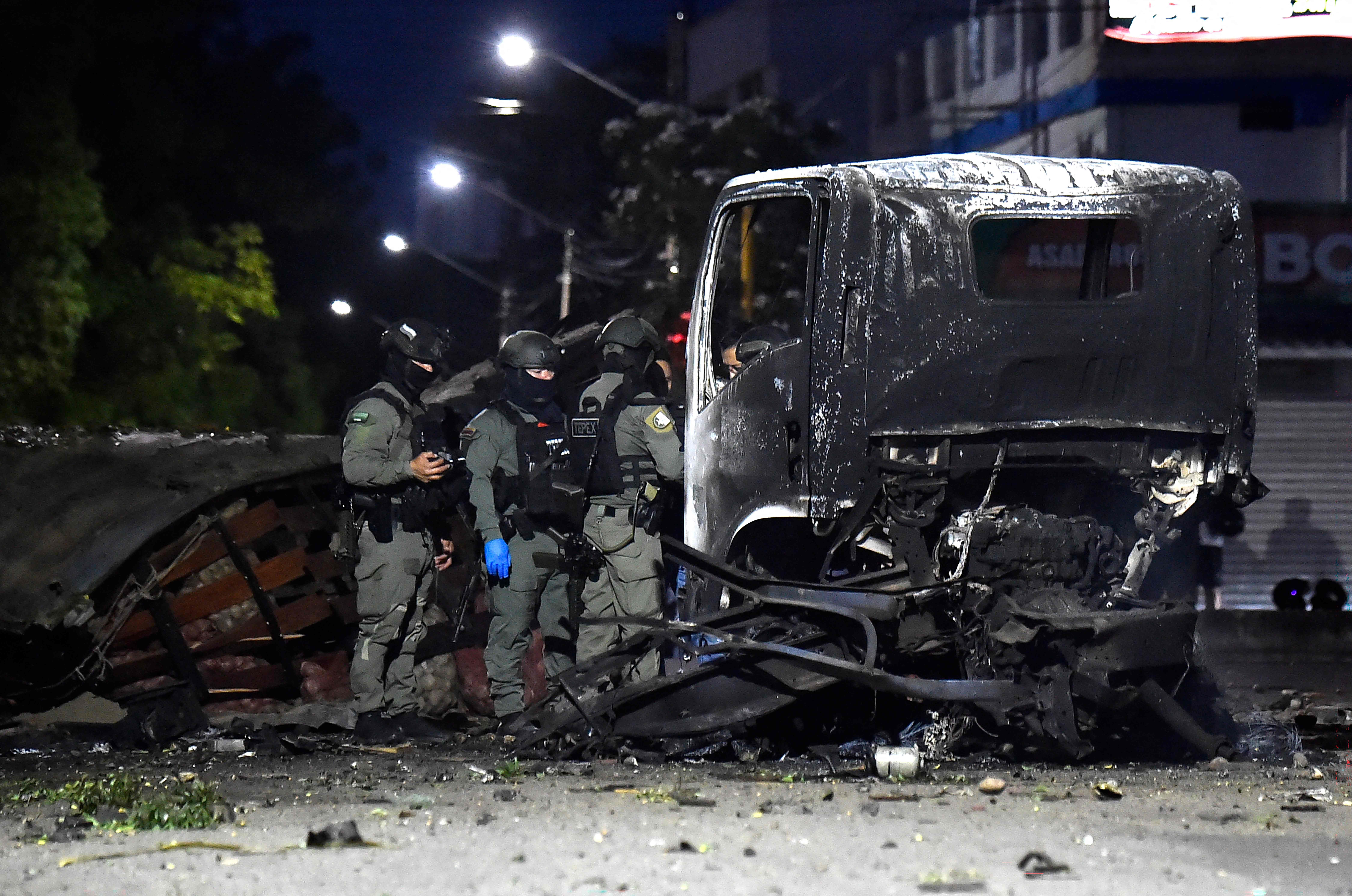 Polizisten untersuchen das Wrack eines ausgebrannten LKWs nach einer Explosion in der Nacht.