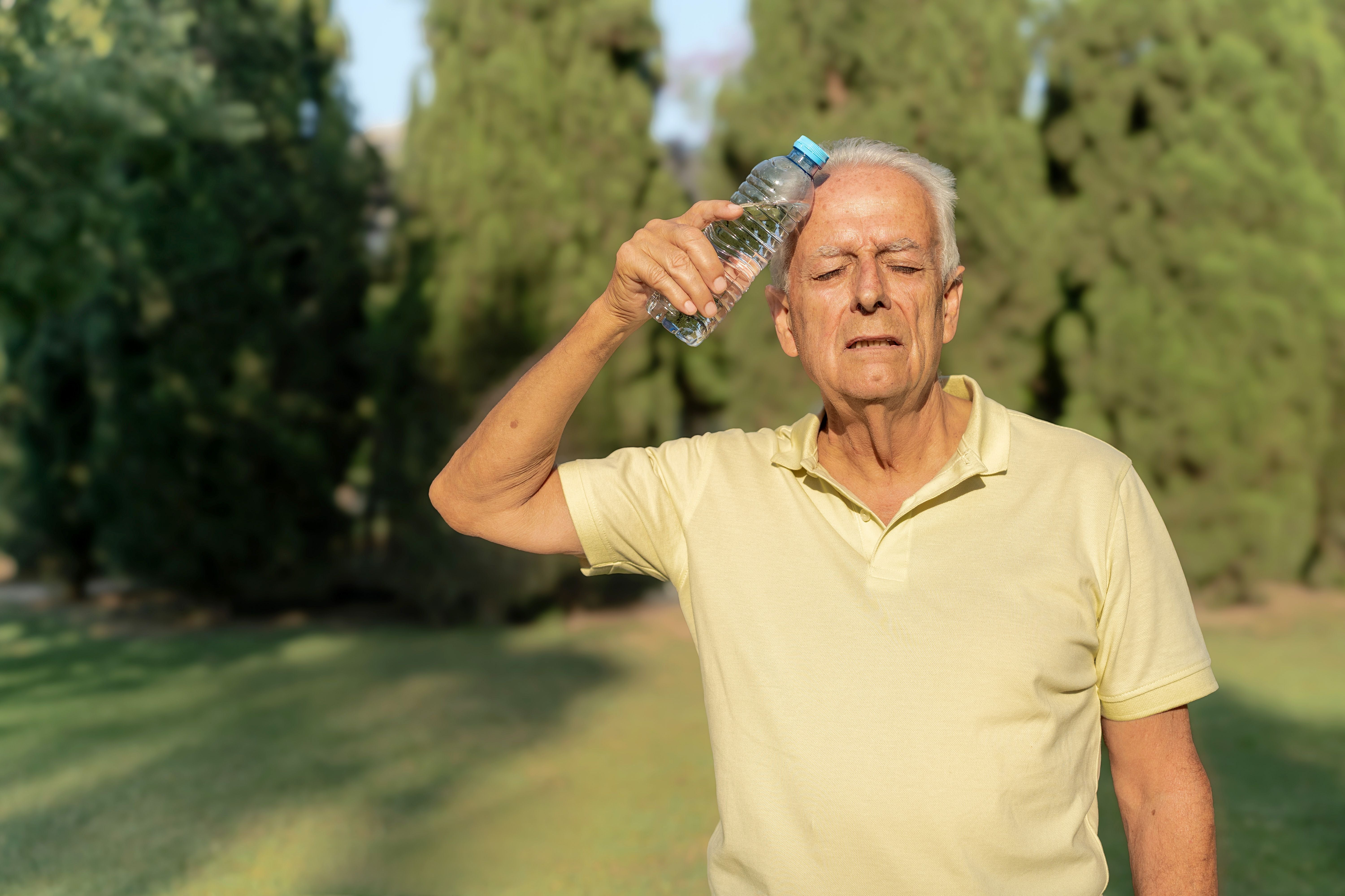 Älterer Mann hält eine Wasserflasche an die Stirn, um sich bei Hitze im Freien abzukühlen.