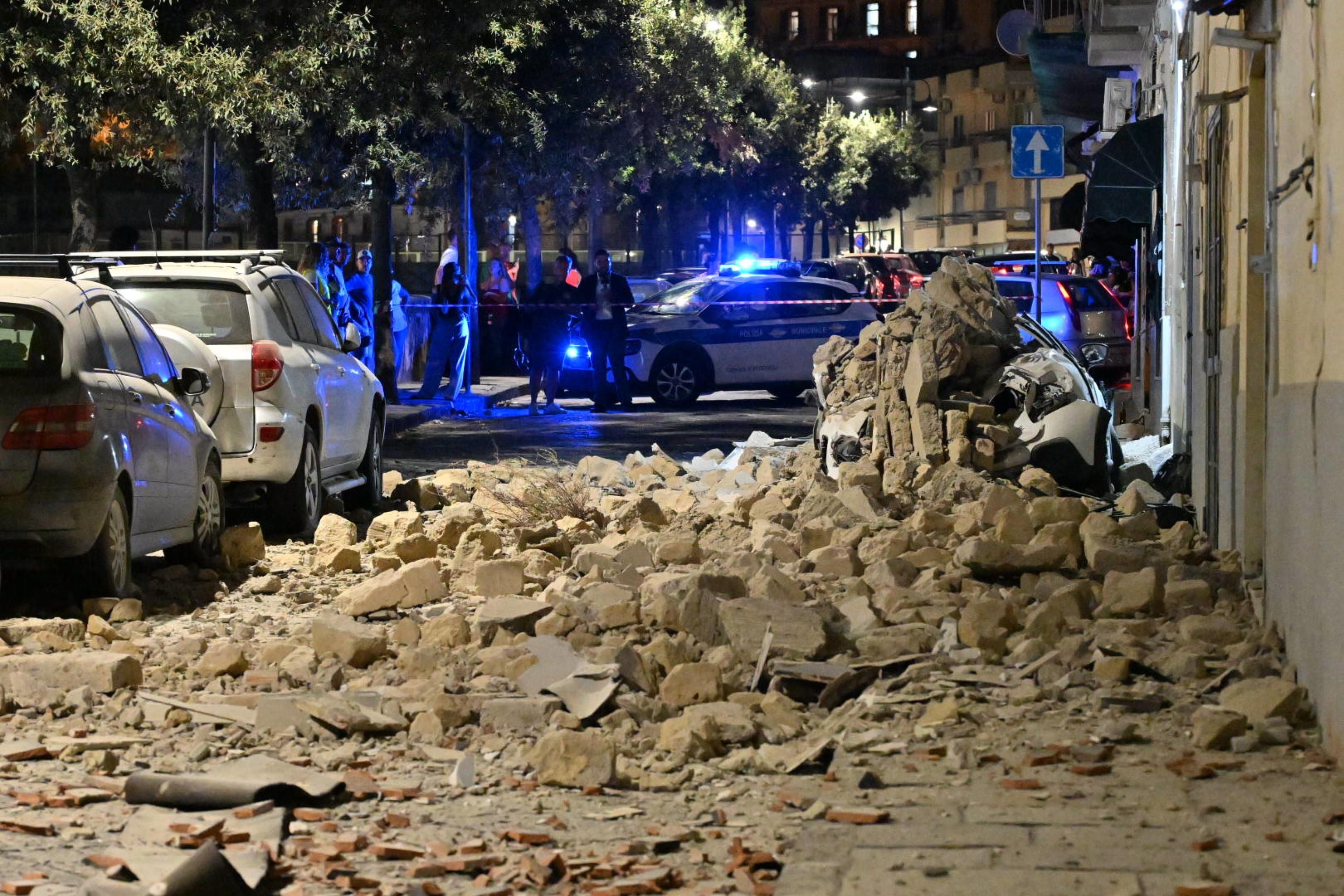 Trümmer und beschädigte Autos nach Erdbeben, Polizei sichert die Straße in Pozzuoli bei Nacht.