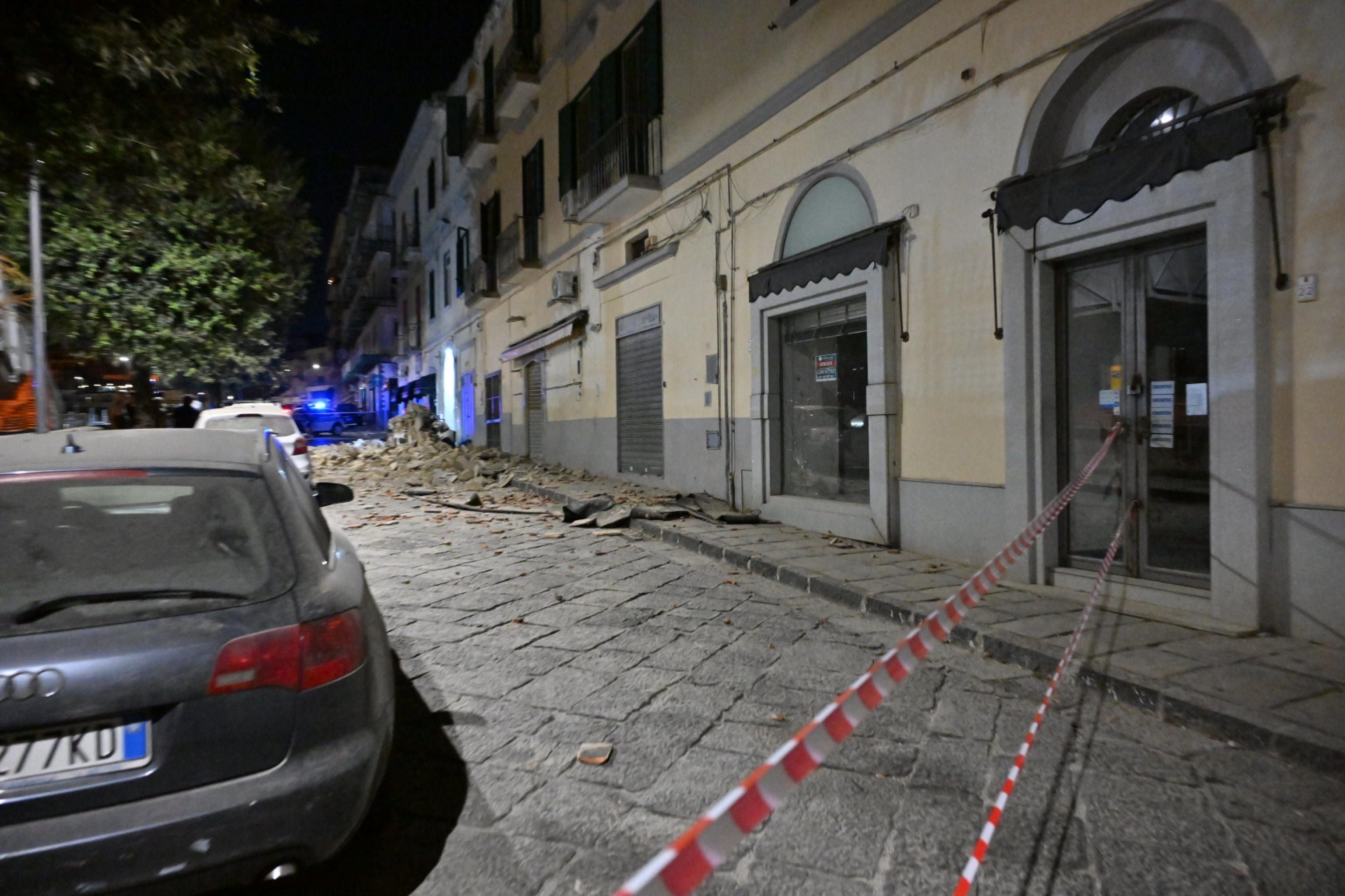 Absperrband vor beschädigten Gebäuden und Trümmern nach einem Erdbeben in einer nächtlichen Straße.