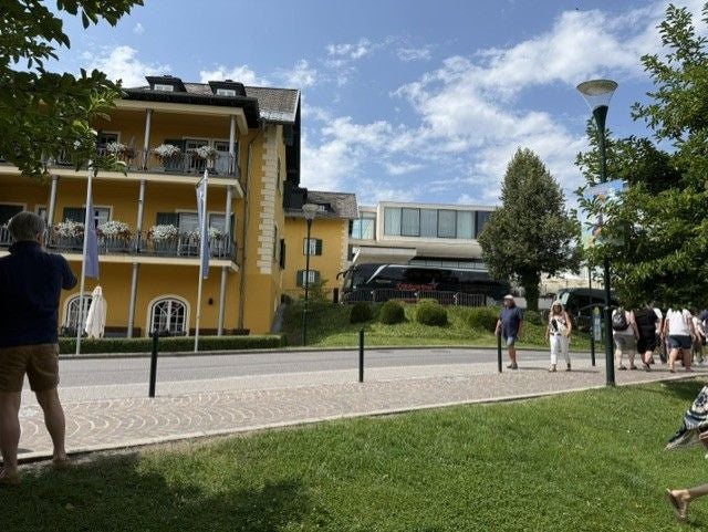 Mehrstöckiges gelbes Gebäude an einer Straße, mehrere Menschen laufen und sonniges Wetter.