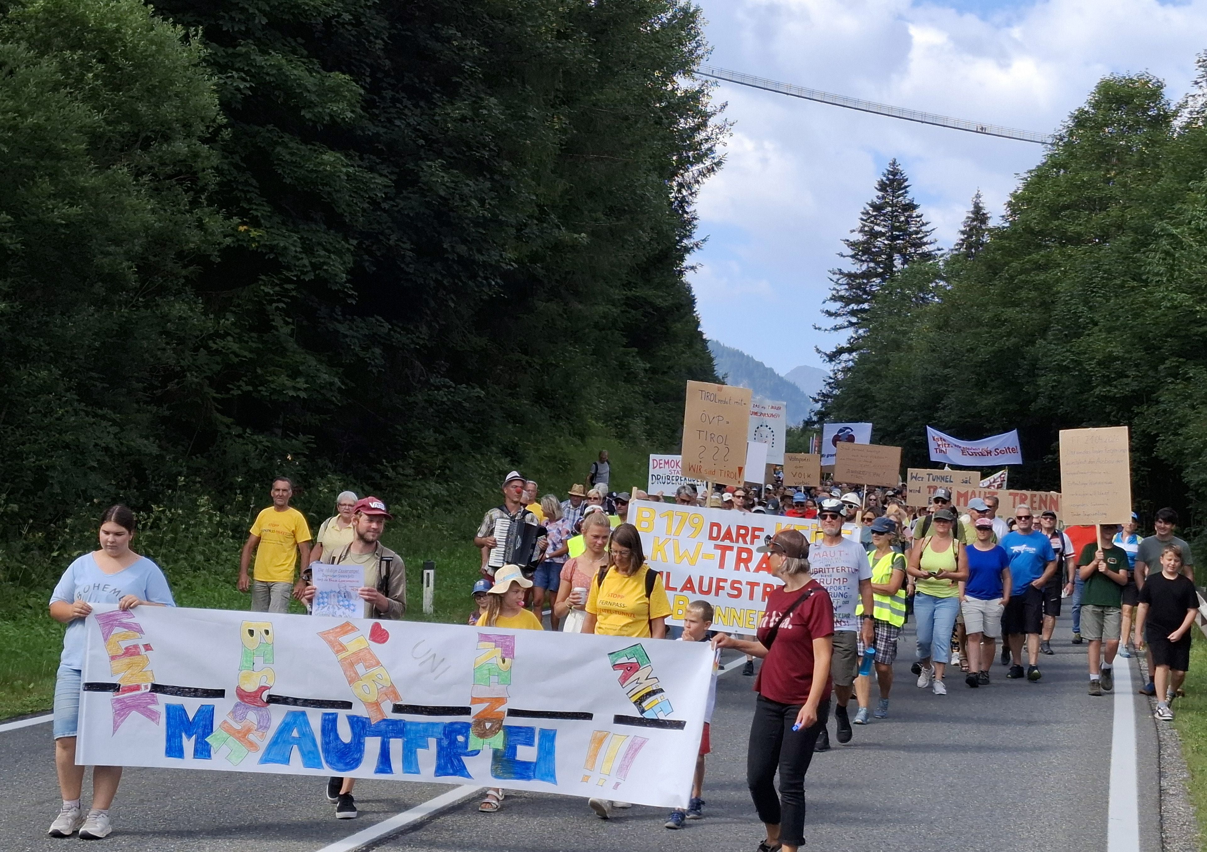 Eine große Gruppe demonstriert auf der Fernpassstraße in Reutte mit Transparenten und Plakaten.
