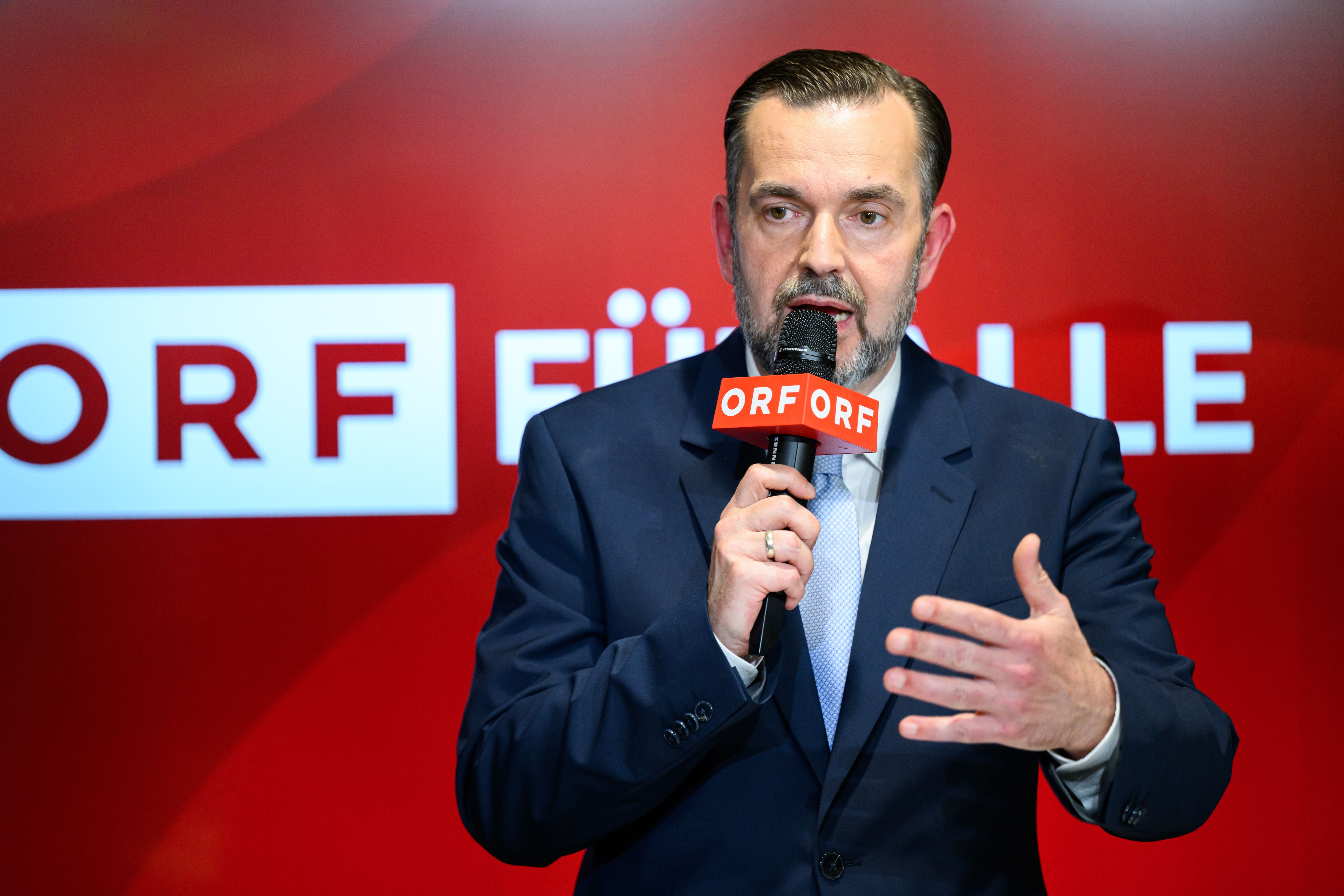 Ein Mann im Anzug spricht bei einer ORF-Veranstaltung in ein Mikrofon mit ORF-Logo.