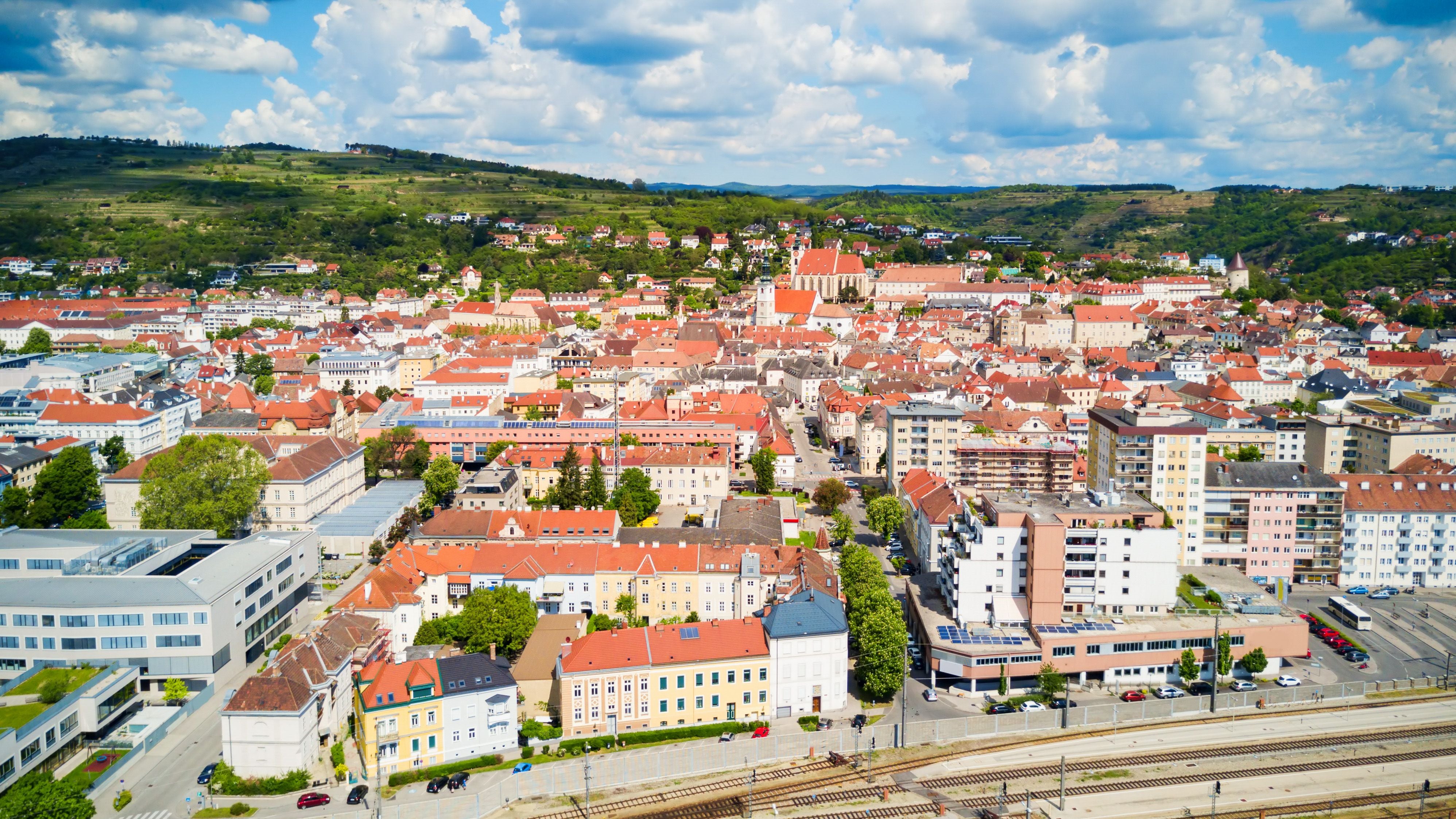 Luftaufnahme von Krems an der Donau mit roten Dächern und umliegenden Hügeln im Hintergrund.