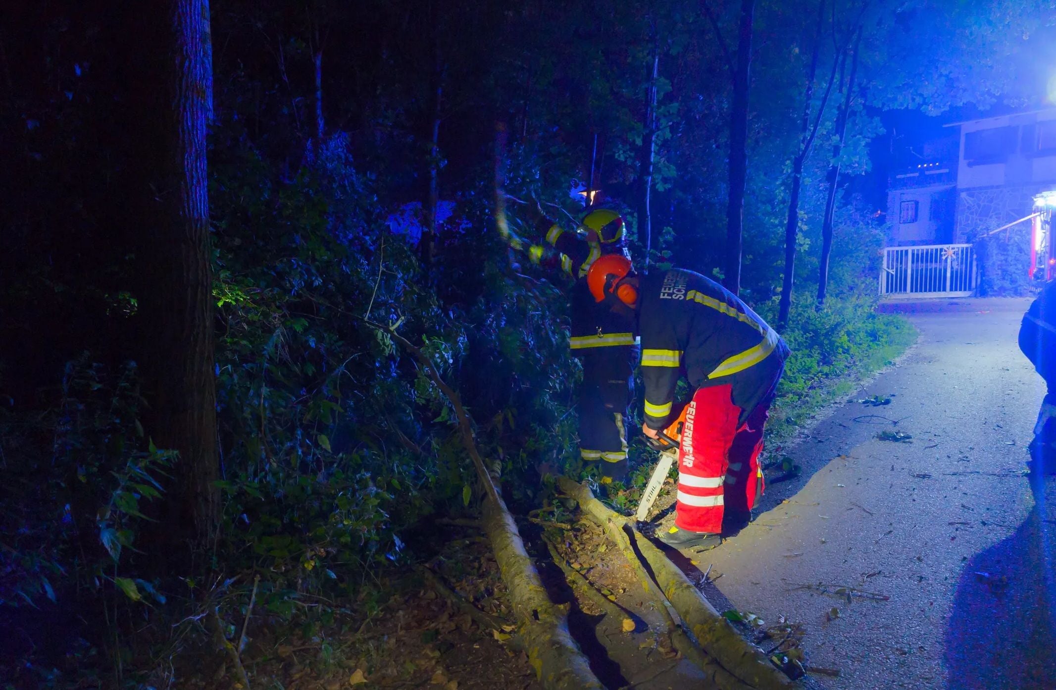 Zwei Feuerwehrleute zersägen bei Nacht einen umgestürzten Baum nach einem Sturm.