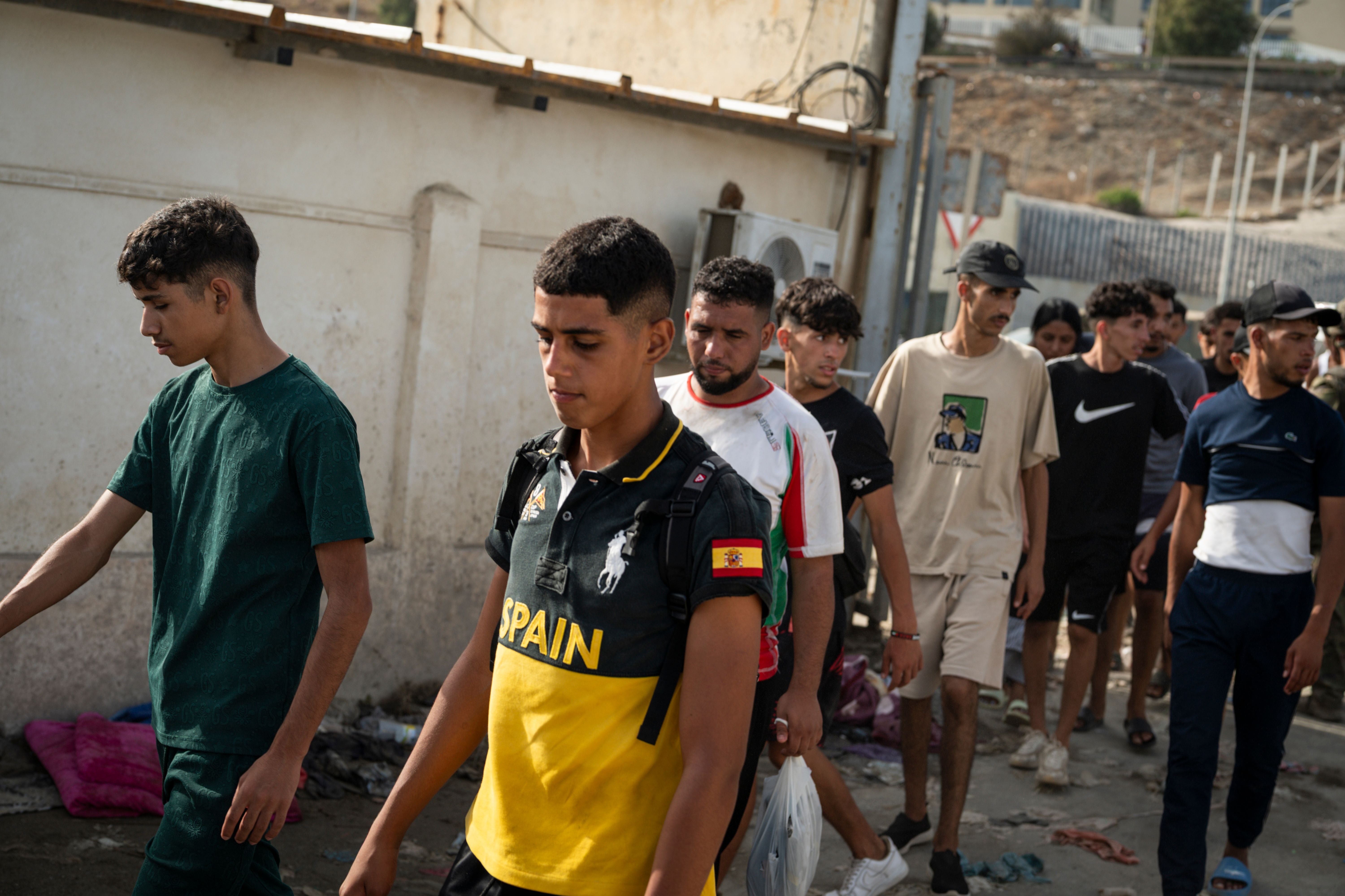 Eine Gruppe junger Migranten läuft an einer Mauer entlang in Ceuta, Spanien, bei Tageslicht.