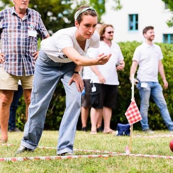 Eine Frau wirft beim Boccia-Spiel eine Kugel, Zuschauer stehen im Hintergrund.