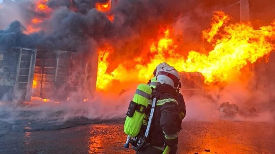 Ein Feuerwehrmann bekämpft einen Großbrand mit dichten Rauch- und Flammenwolken.