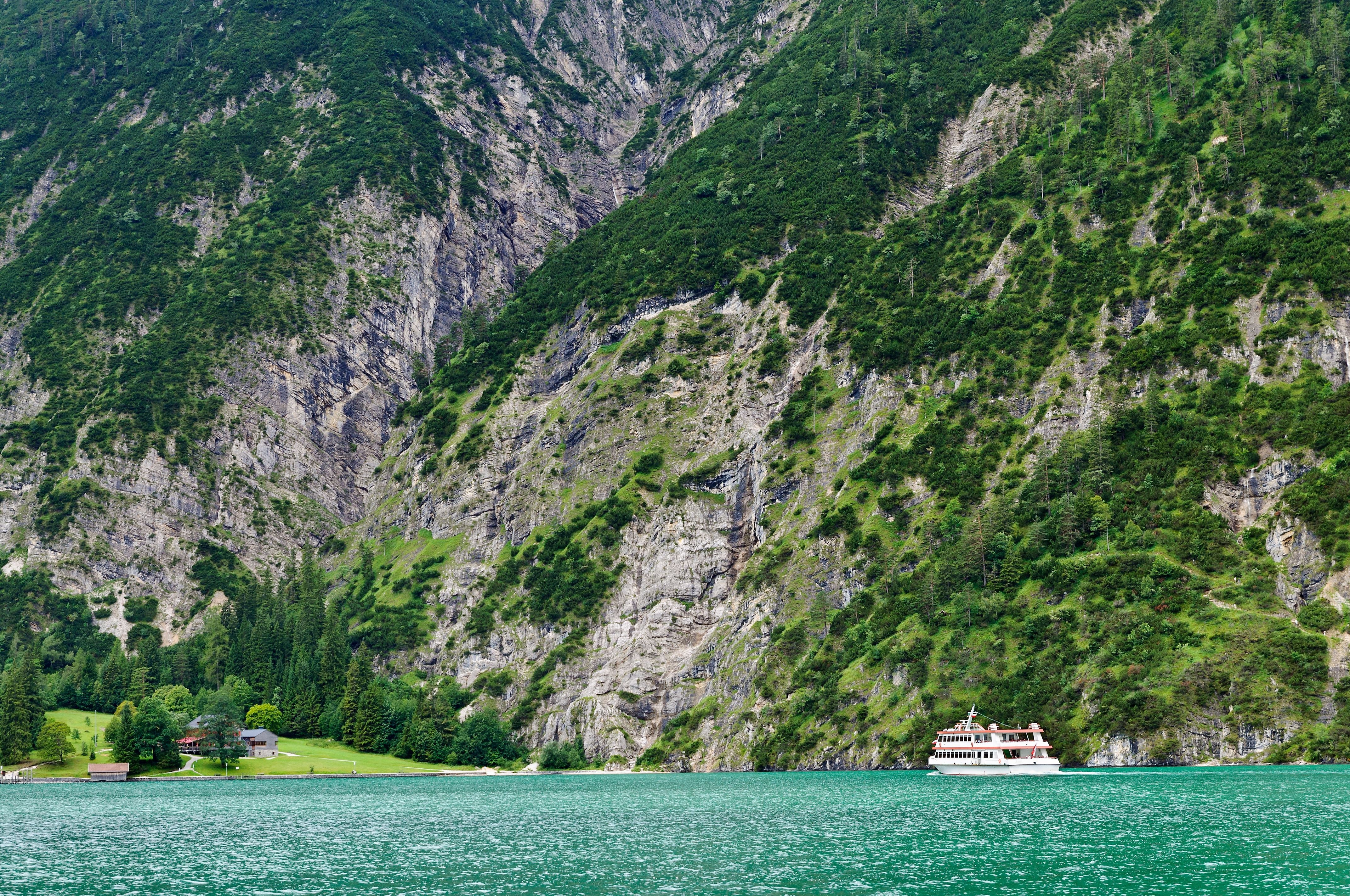 Weiße Fähre fährt vor steilen, bewaldeten Bergen am türkisfarbenen Achensee entlang.