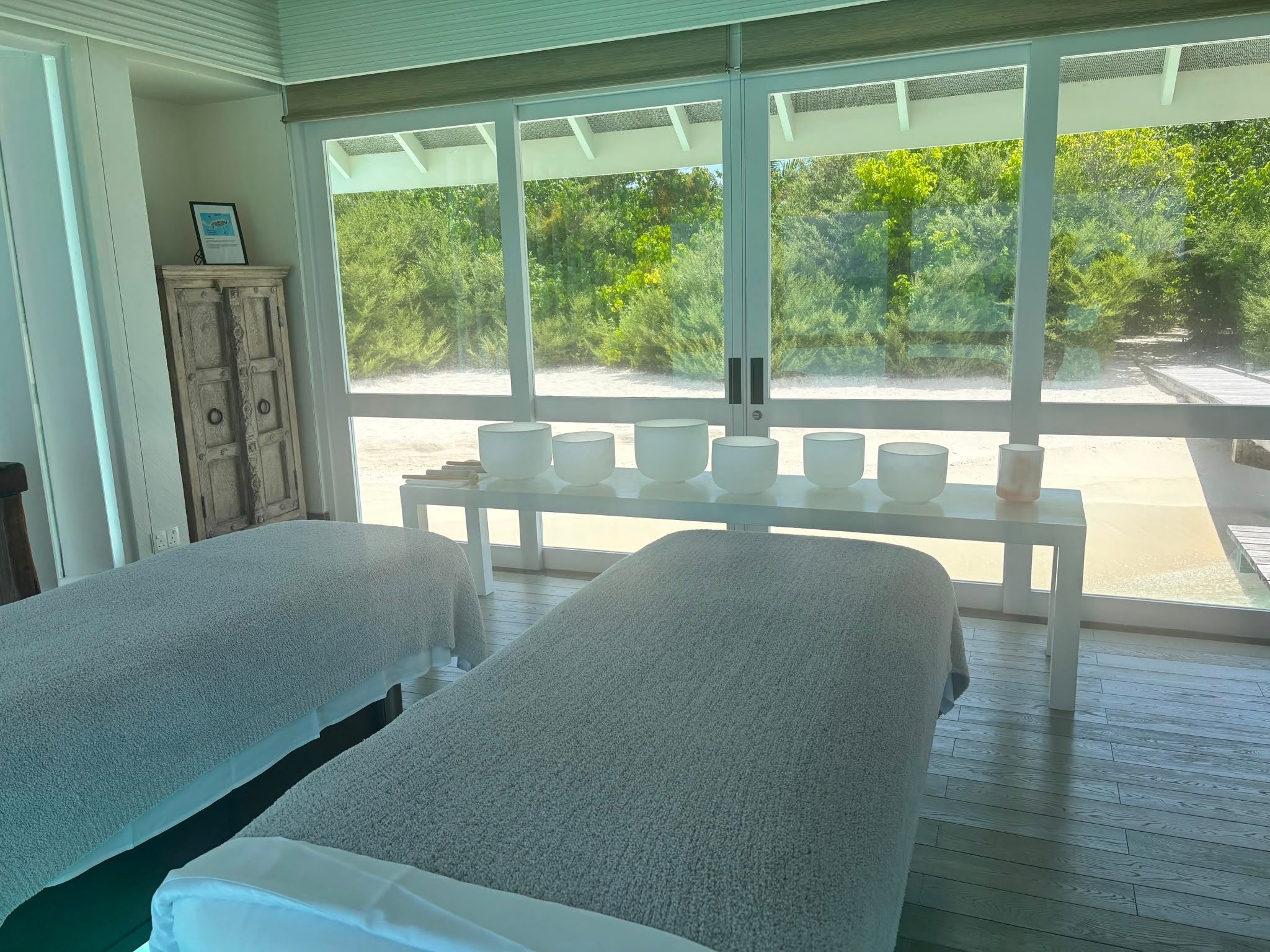 Zwei Massageliegen im Spa mit Blick auf Garten und Strand durch große Fenster.