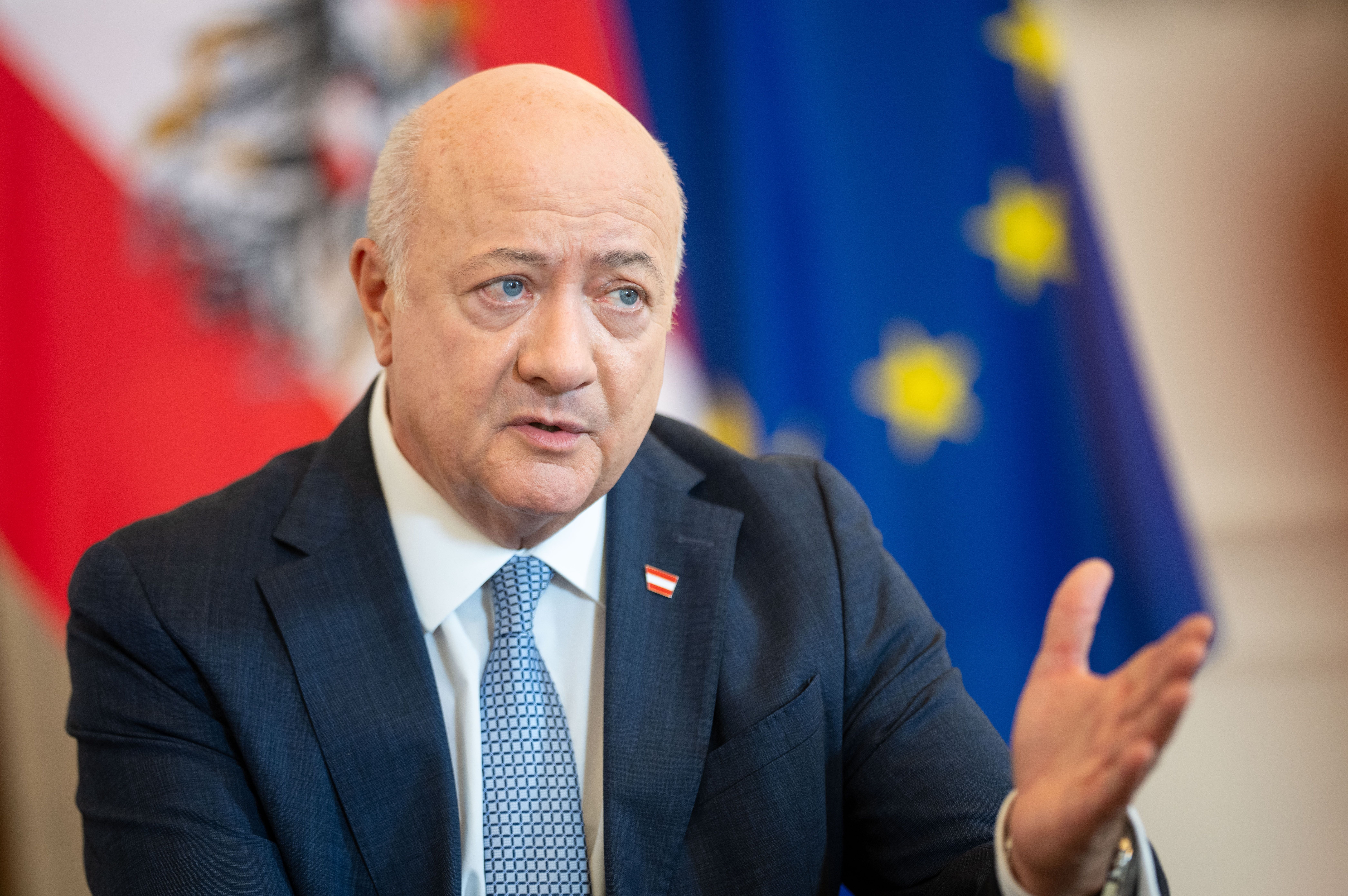 Ein Mann im Anzug spricht gestikulierend vor österreichischer und EU-Flagge.