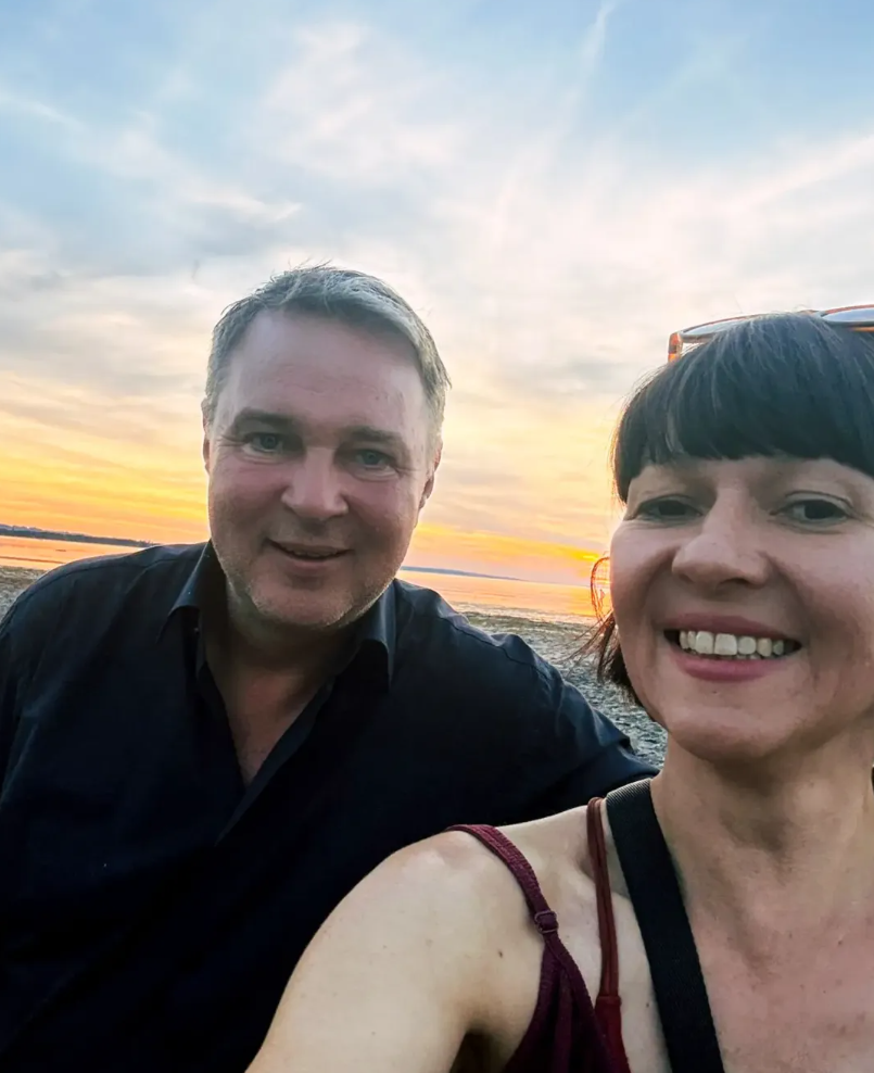 Zwei Menschen machen ein Selfie am Strand bei Sonnenuntergang.