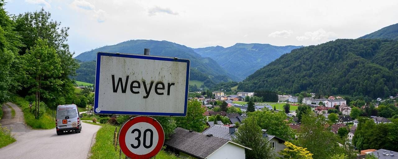 Ortsschild von Weyer vor einer Stadt im Tal, umgeben von bewaldeten Bergen und einer 30er-Zone.