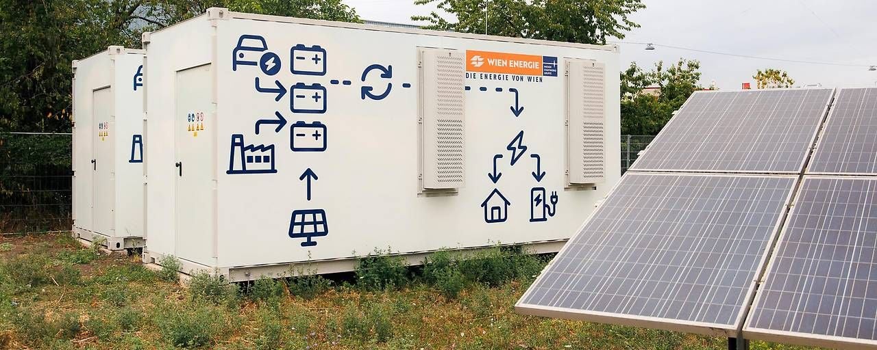 Container mit Grafiken zur Energiespeicherung, daneben Solarpanele auf einer Wiese.