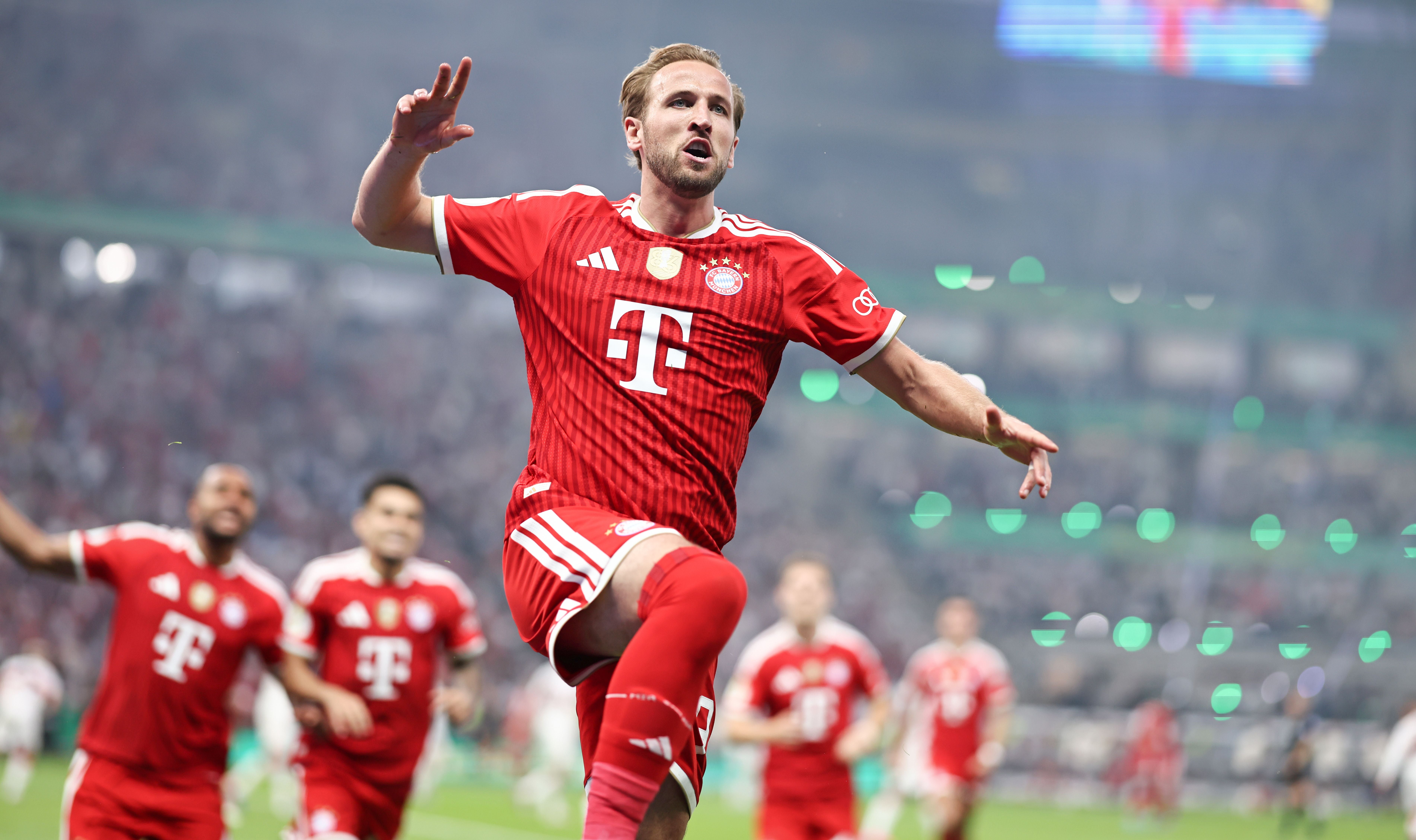 Ein Fußballspieler des FC Bayern jubelt nach einem Tor im Stadion, Teamkollegen im Hintergrund.