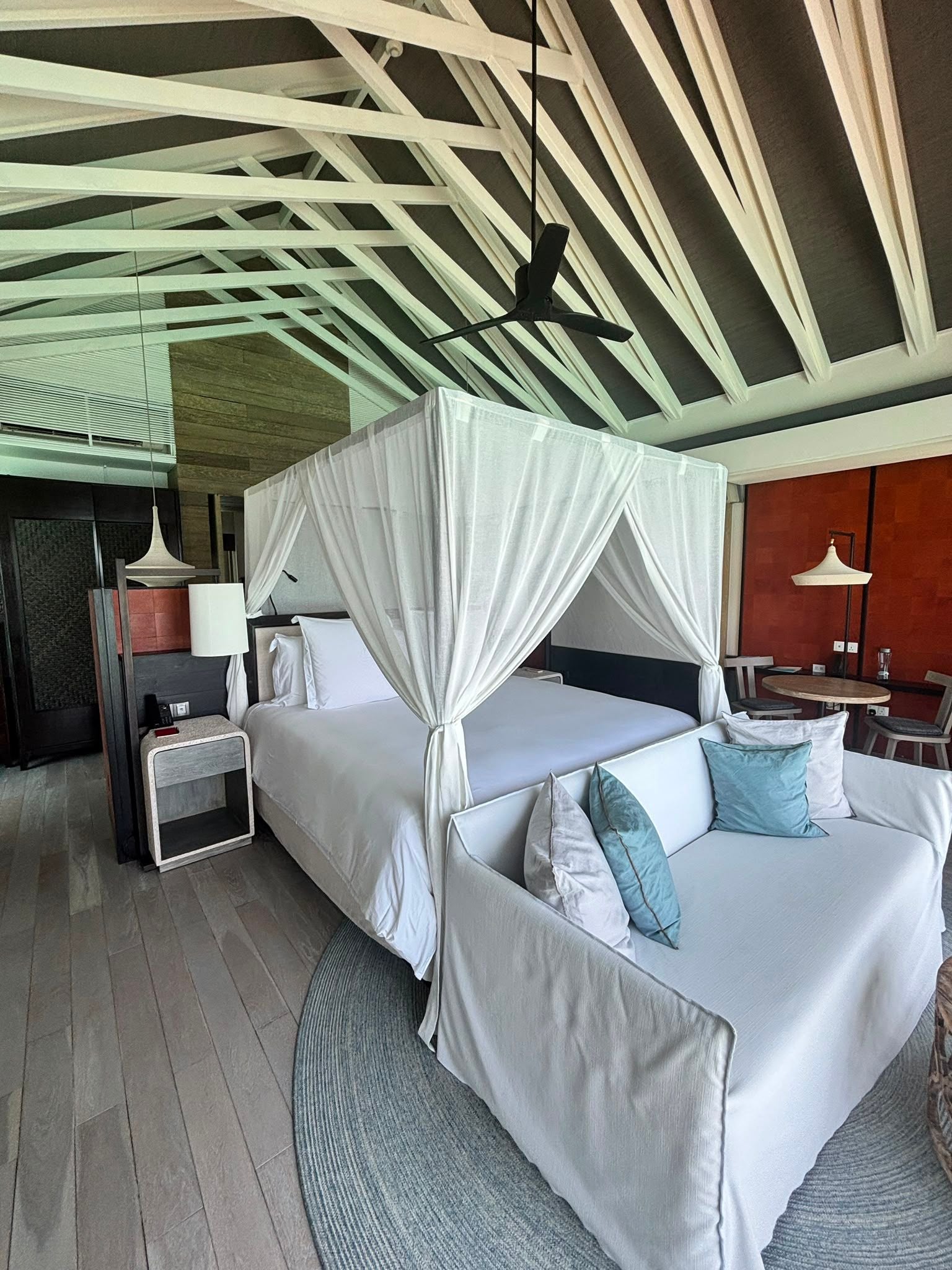 Modernes Zimmer mit Himmelbett, Sofa und hoher Decke mit sichtbaren weißen Balken.