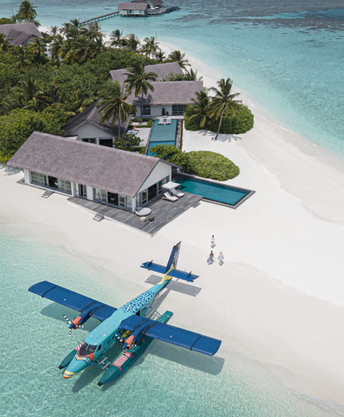 Luxuriöser Strandbungalow mit Pool, Palmen und Wasserflugzeug auf weißem Sandstrand.