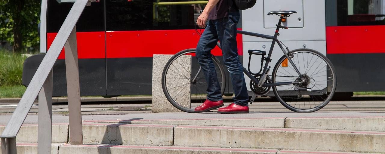 Mann mit Fahrrad steht vor einer Straßenbahn an einer Haltestelle.
