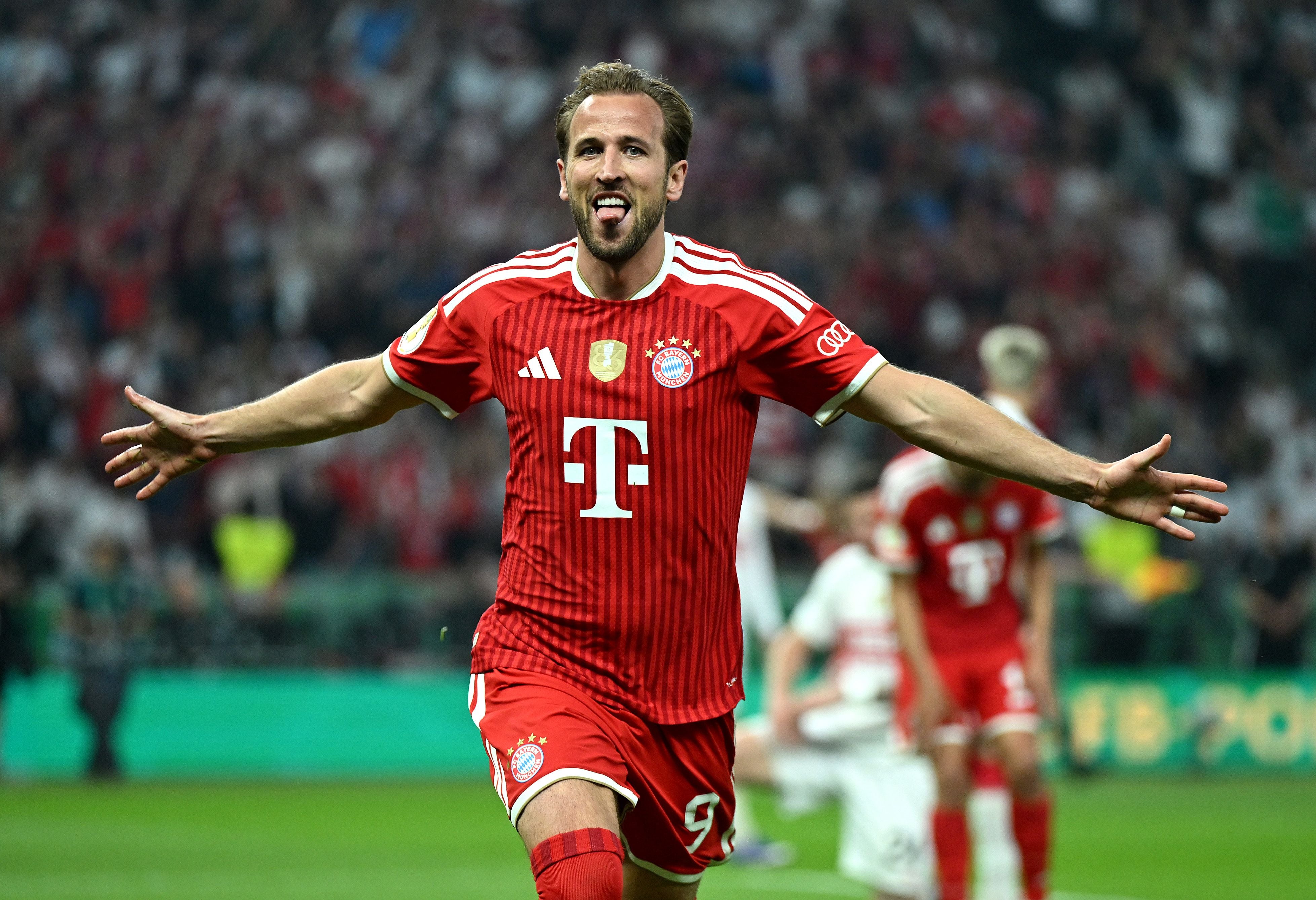 Ein Fußballspieler im roten FC Bayern-Trikot jubelt mit ausgebreiteten Armen auf dem Spielfeld.