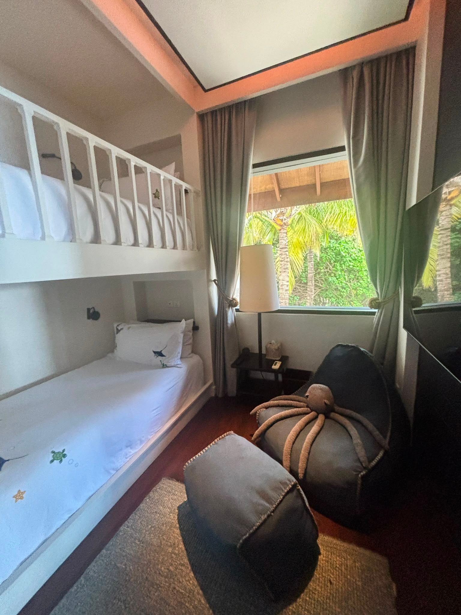 Gemütliches Zimmer mit Etagenbett, Sitzsack und Fenster mit Blick auf Palmen im Garten.