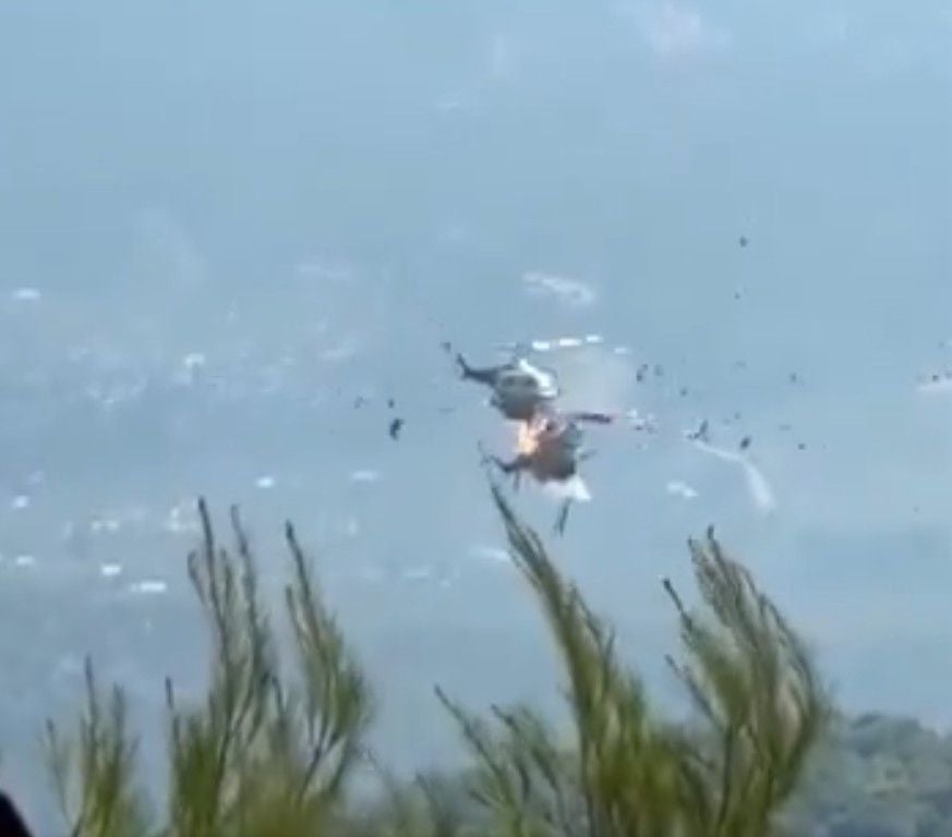 Zwei Hubschrauber kollidieren in der Luft, Trümmerteile und Feuer sind sichtbar.