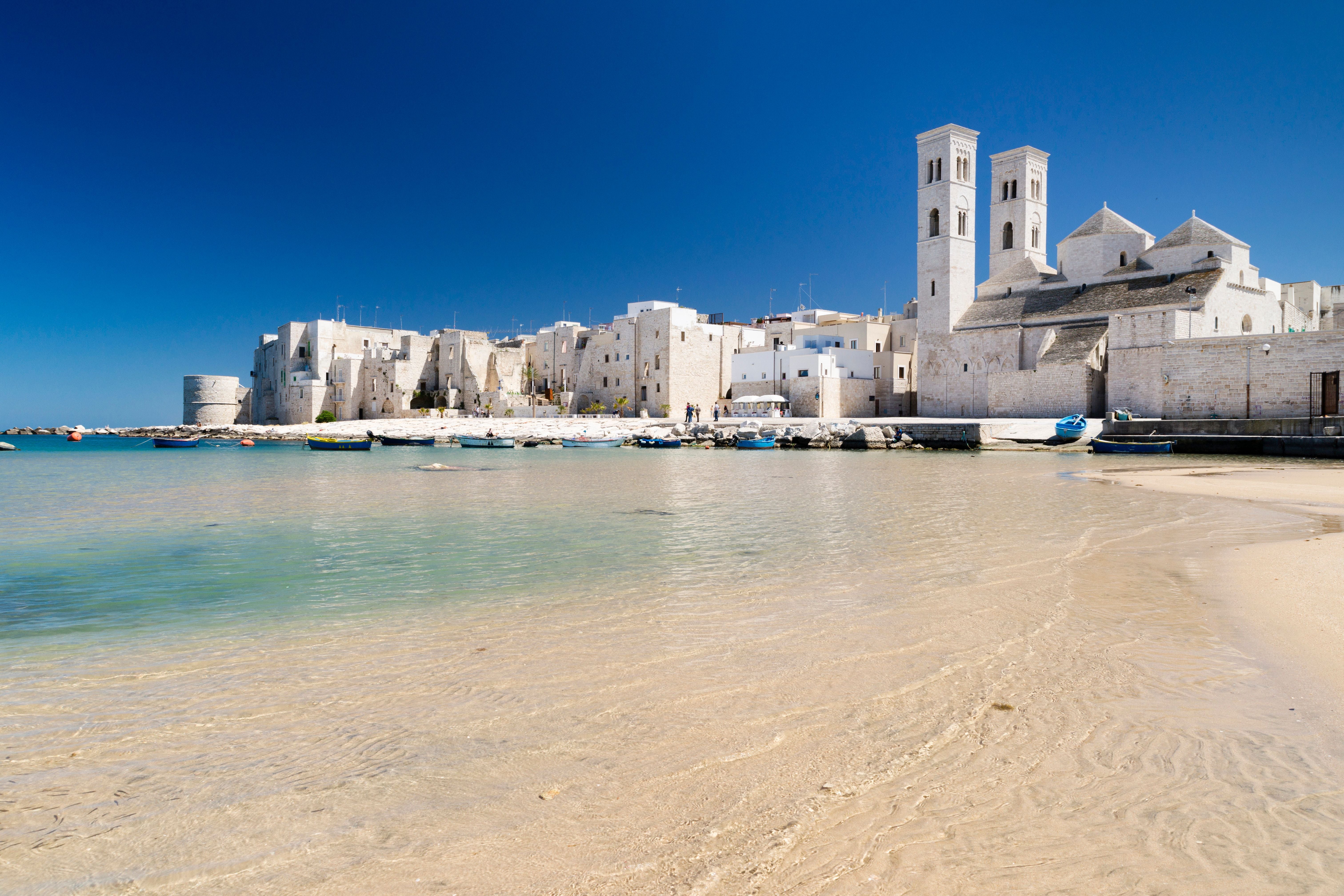 Historische Altstadt von Molfetta mit Kathedrale und Fischerbooten am klaren Sandstrand.