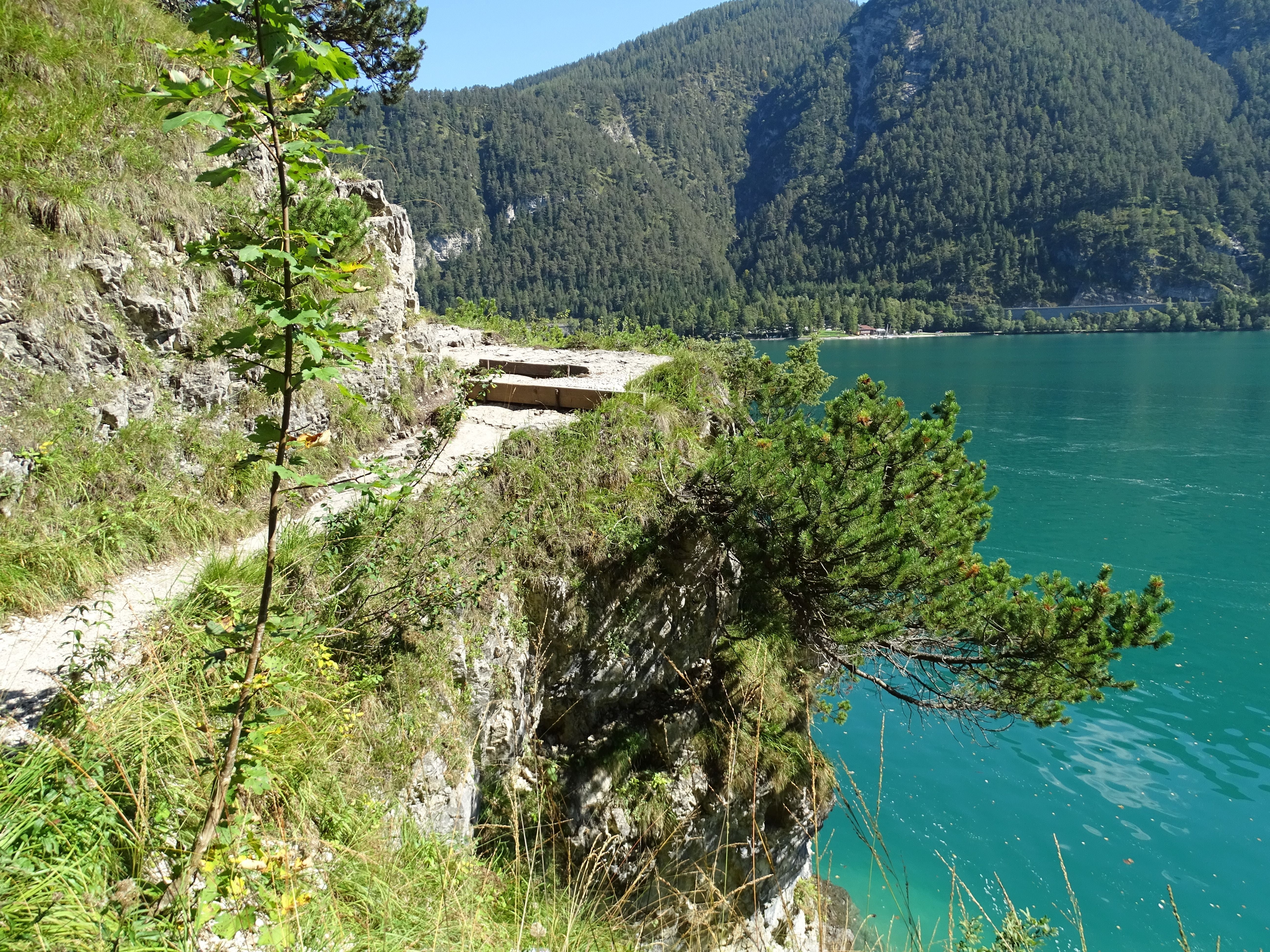 Bergpfad am türkisfarbenen See mit grünen Alpenhängen im Sommer.