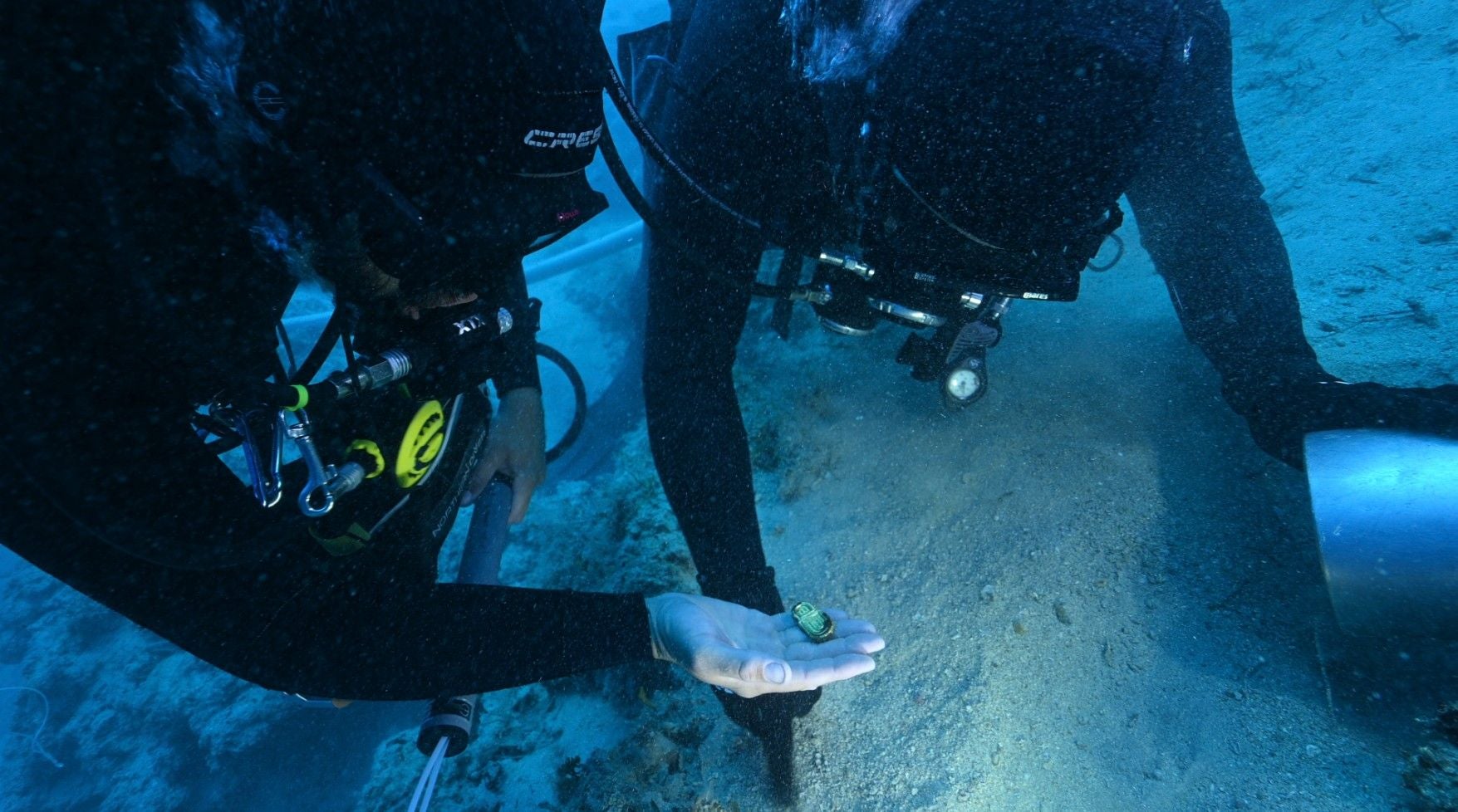 Zwei Taucher finden unter Wasser ein goldenes Artefakt aus einem alten Schiffswrack.