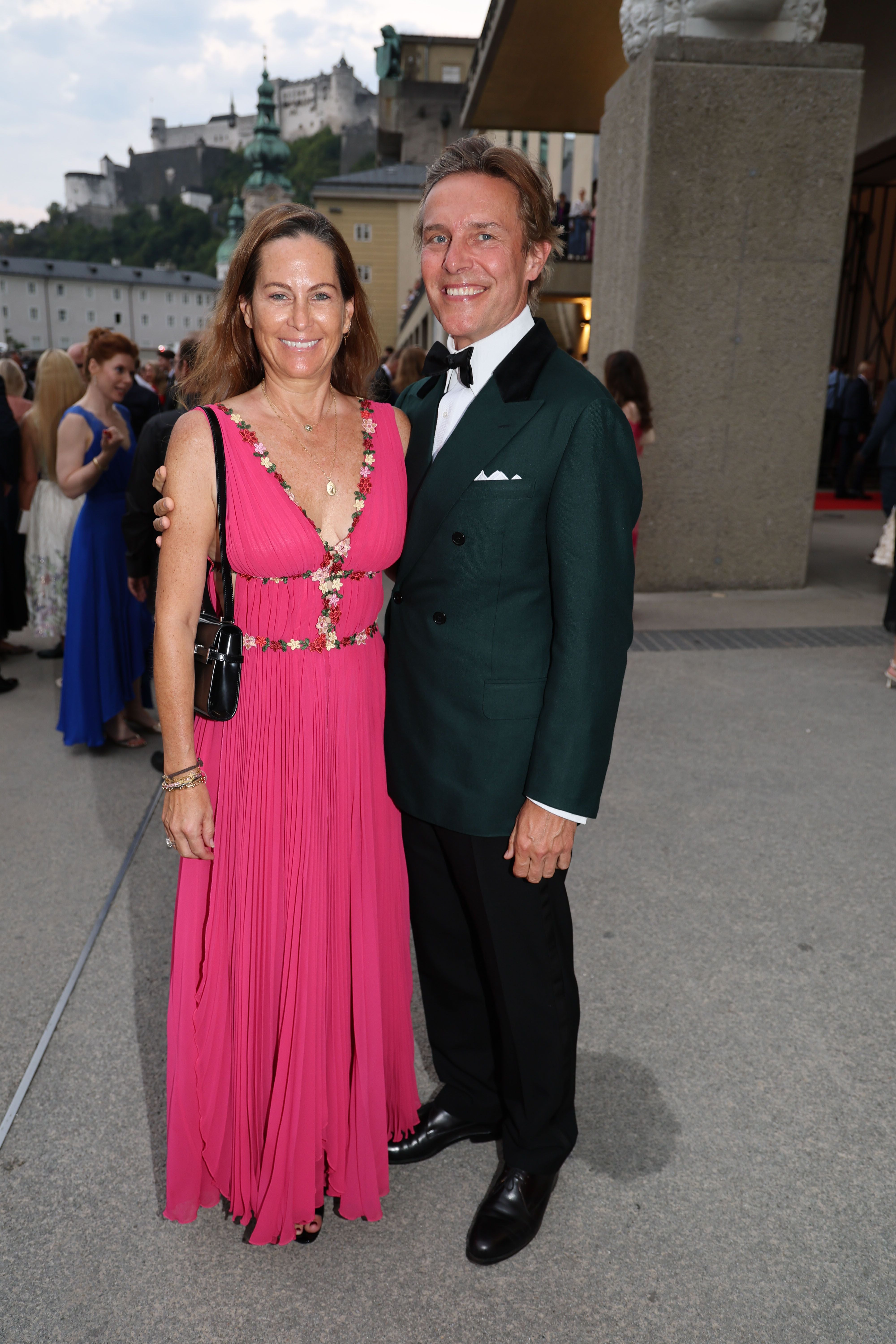 Eine Frau im pinken Kleid und ein Mann im Smoking posieren lächelnd bei den Salzburger Festspielen.