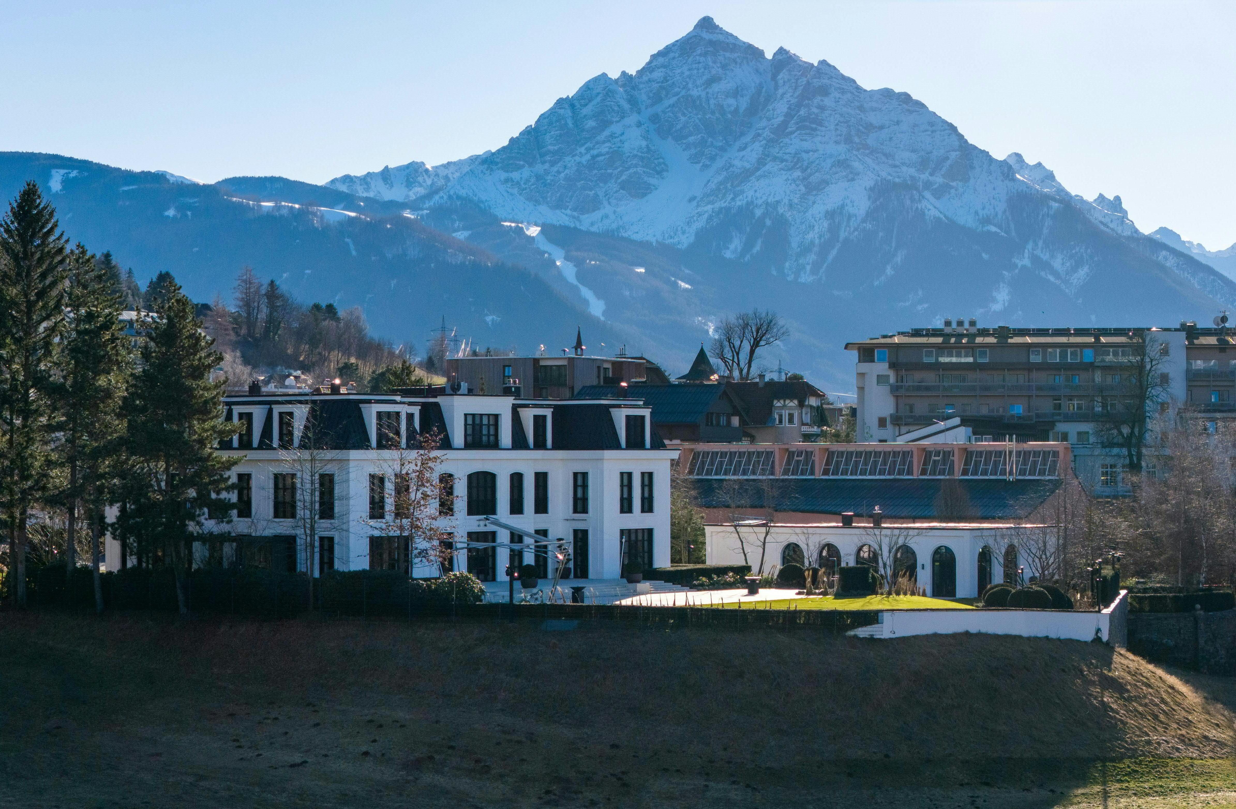 Weiße Villa mit Garten vor verschneiten Bergen in Innsbruck, umgeben von weiteren Gebäuden.