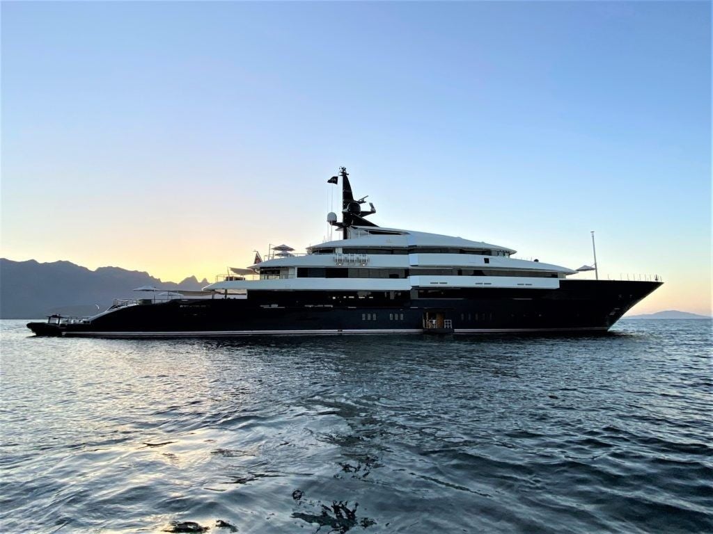 Große Luxusyacht fährt auf dem Meer bei Sonnenuntergang, Berge im Hintergrund.