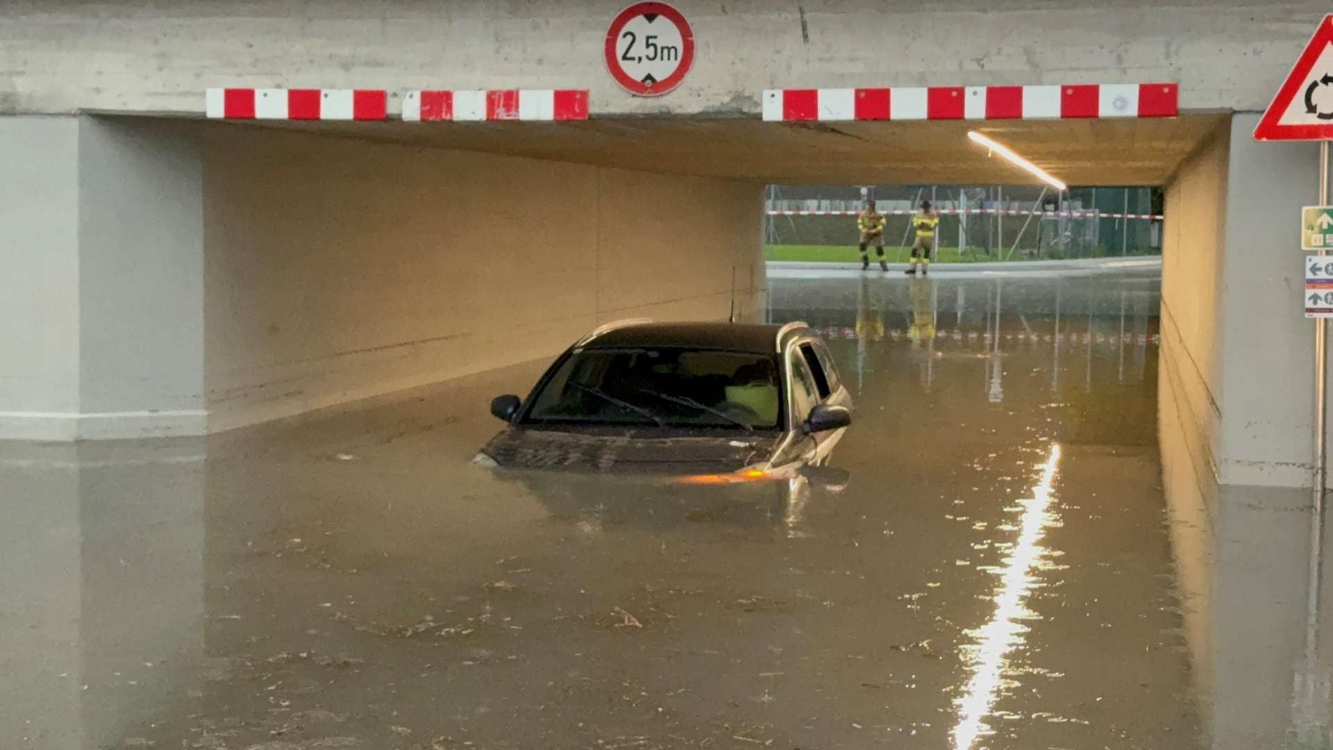 Ein Auto steht in einer überfluteten Unterführung, Wasser reicht bis zur Motorhaube.