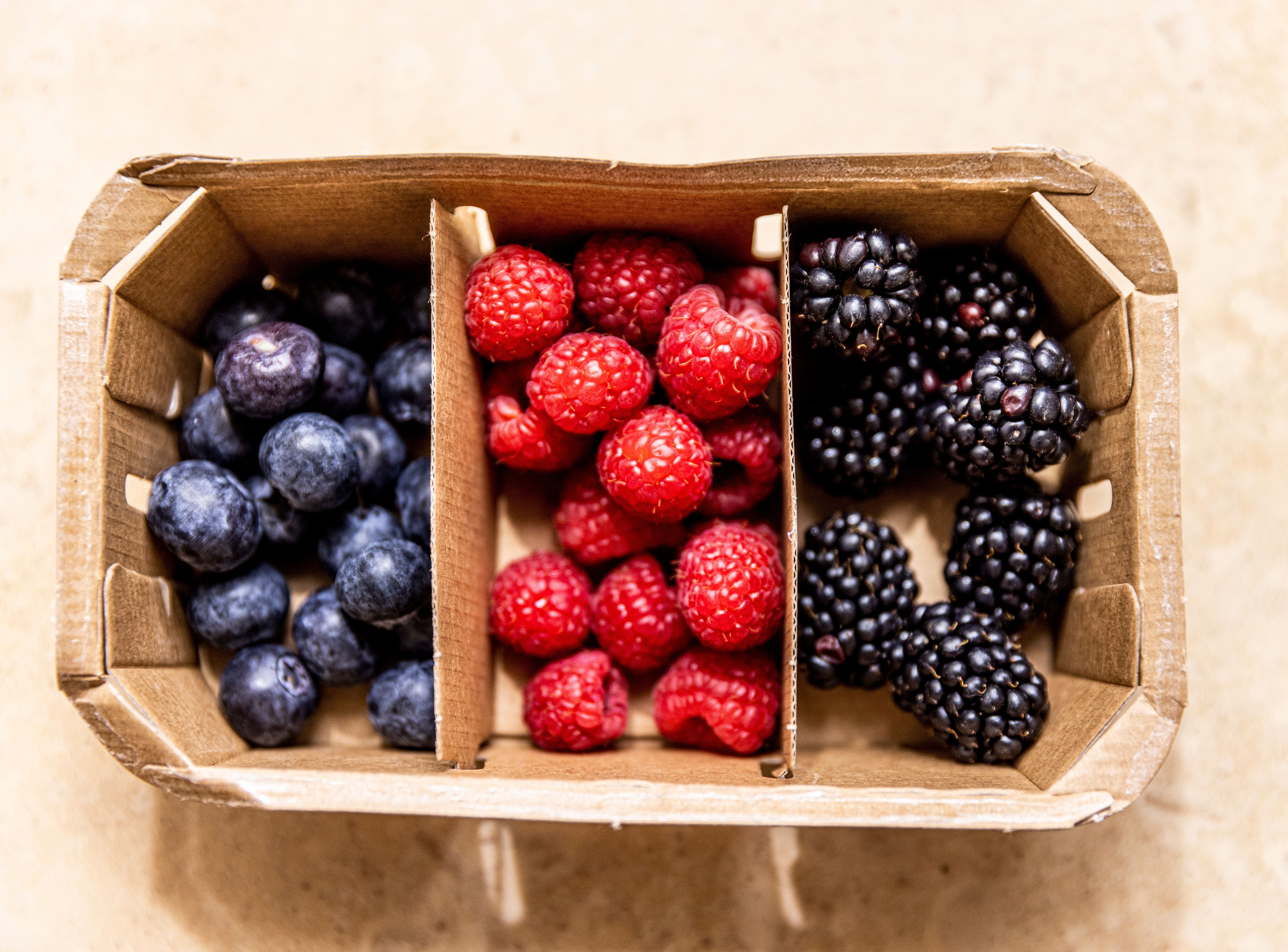 Blaubeeren, Himbeeren und Brombeeren getrennt in einem Karton aus der Vogelperspektive.
