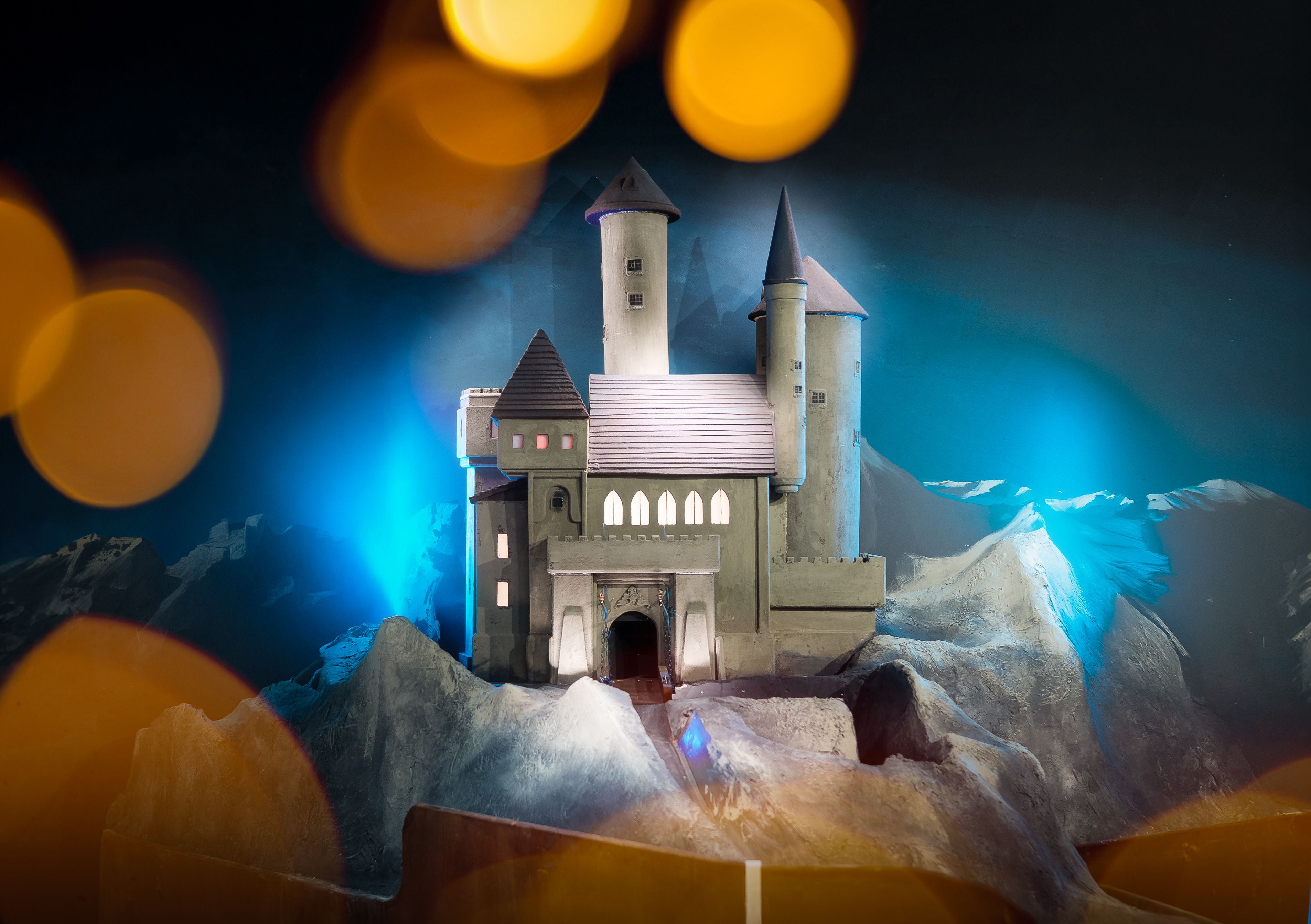 Modell einer beleuchteten Burg auf Felsen, umgeben von blauen und orangefarbenen Lichtern.
