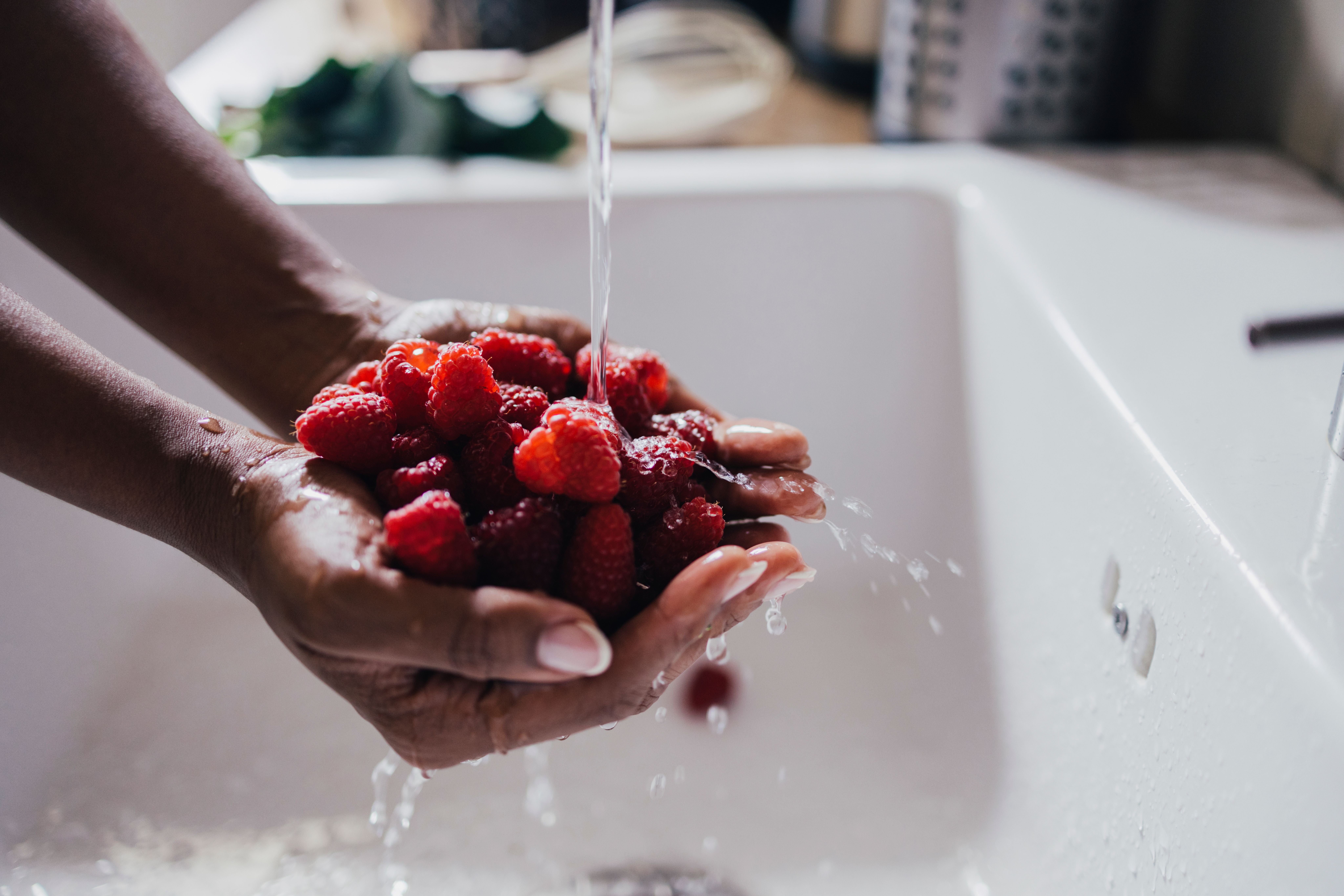 Eine Person wäscht frische Himbeeren unter fließendem Wasser in einem Waschbecken.
