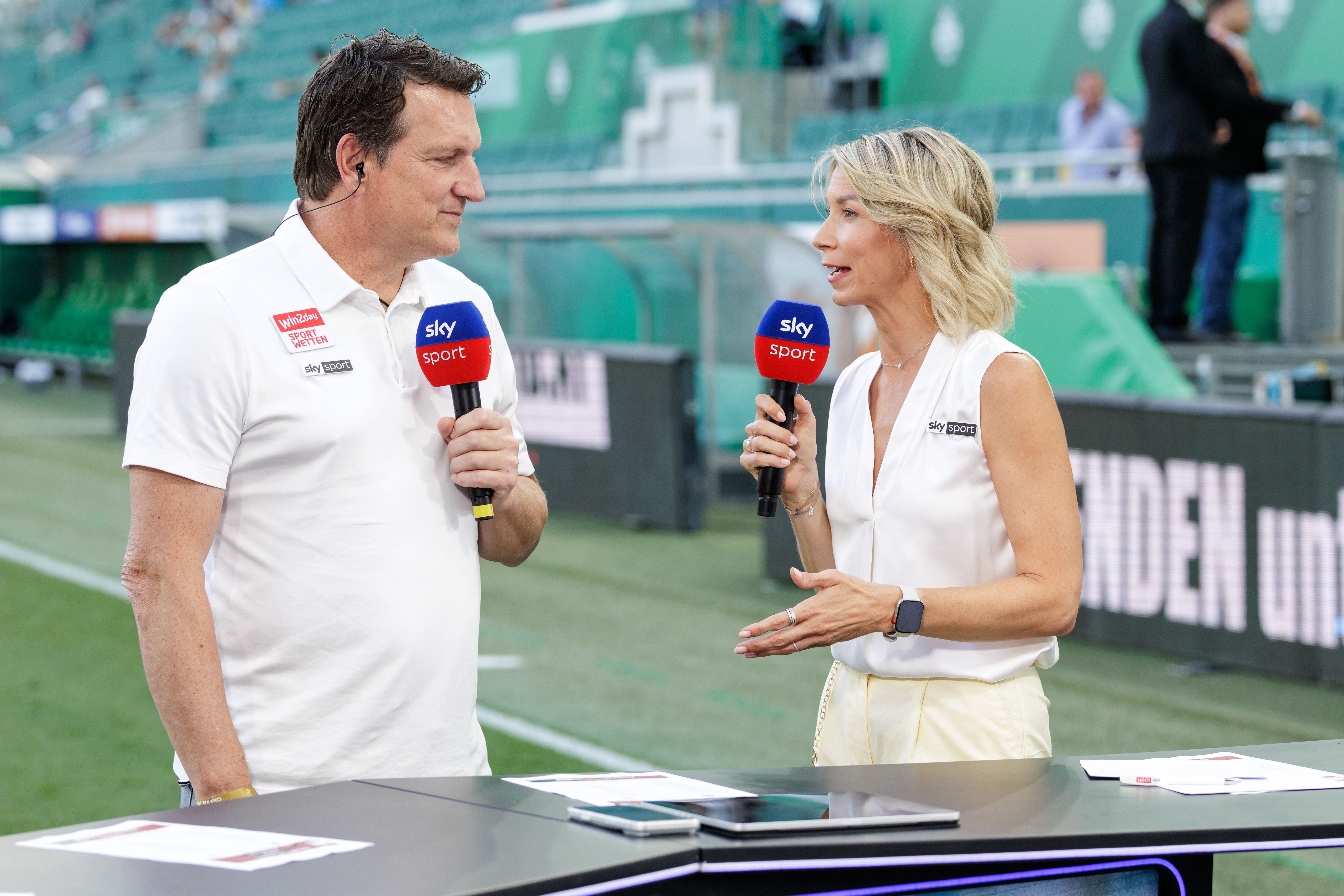 Ein Mann und eine Frau moderieren ein Fußballspiel für Sky Sport im Stadion.