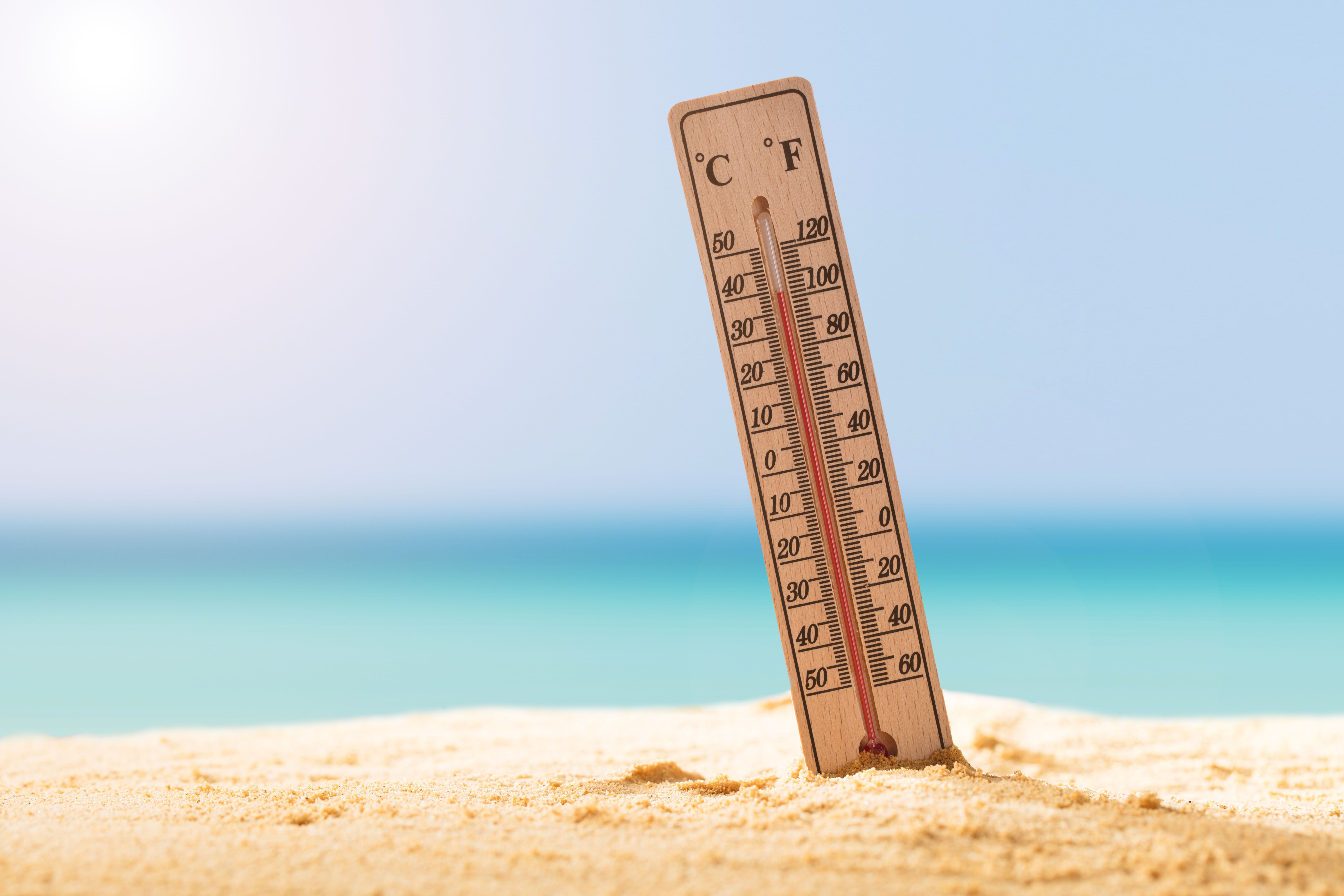 Thermometer steckt im Sand am Strand und zeigt hohe Temperatur bei sonnigem Wetter.
