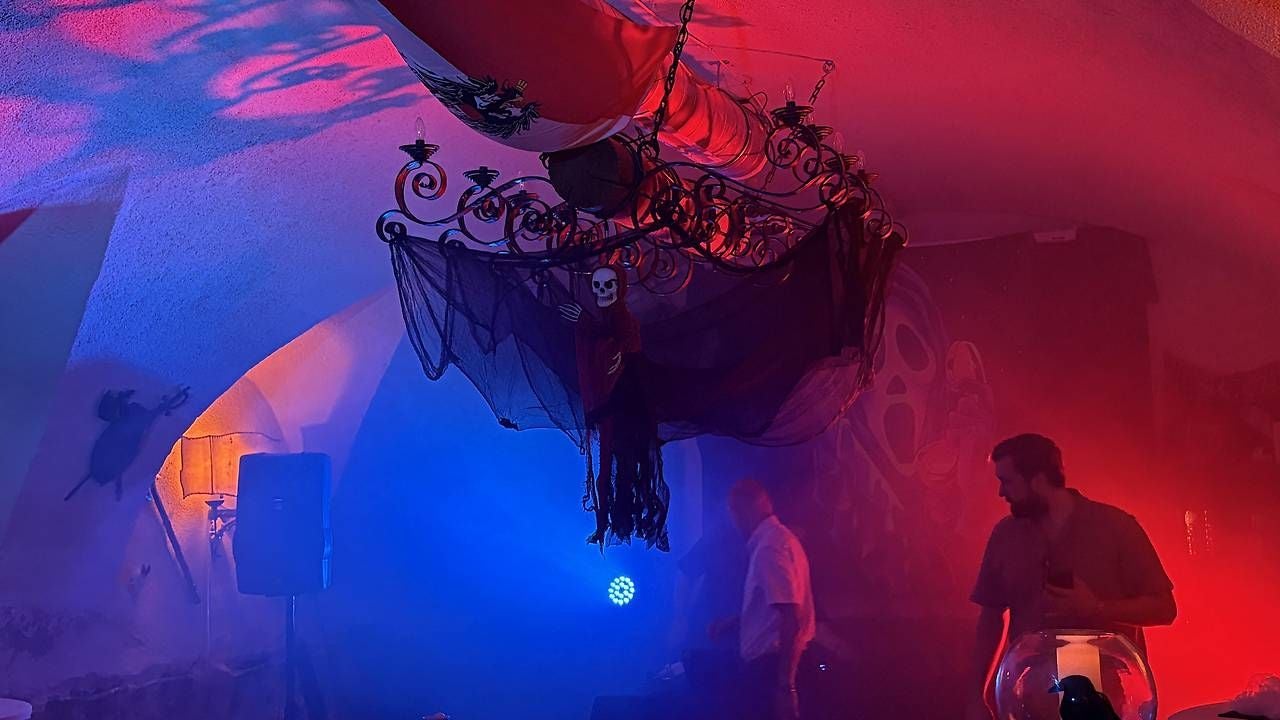 Dunkel beleuchteter Raum mit Halloween-Dekoration, rotem Licht und Skelett an einem Kronleuchter.