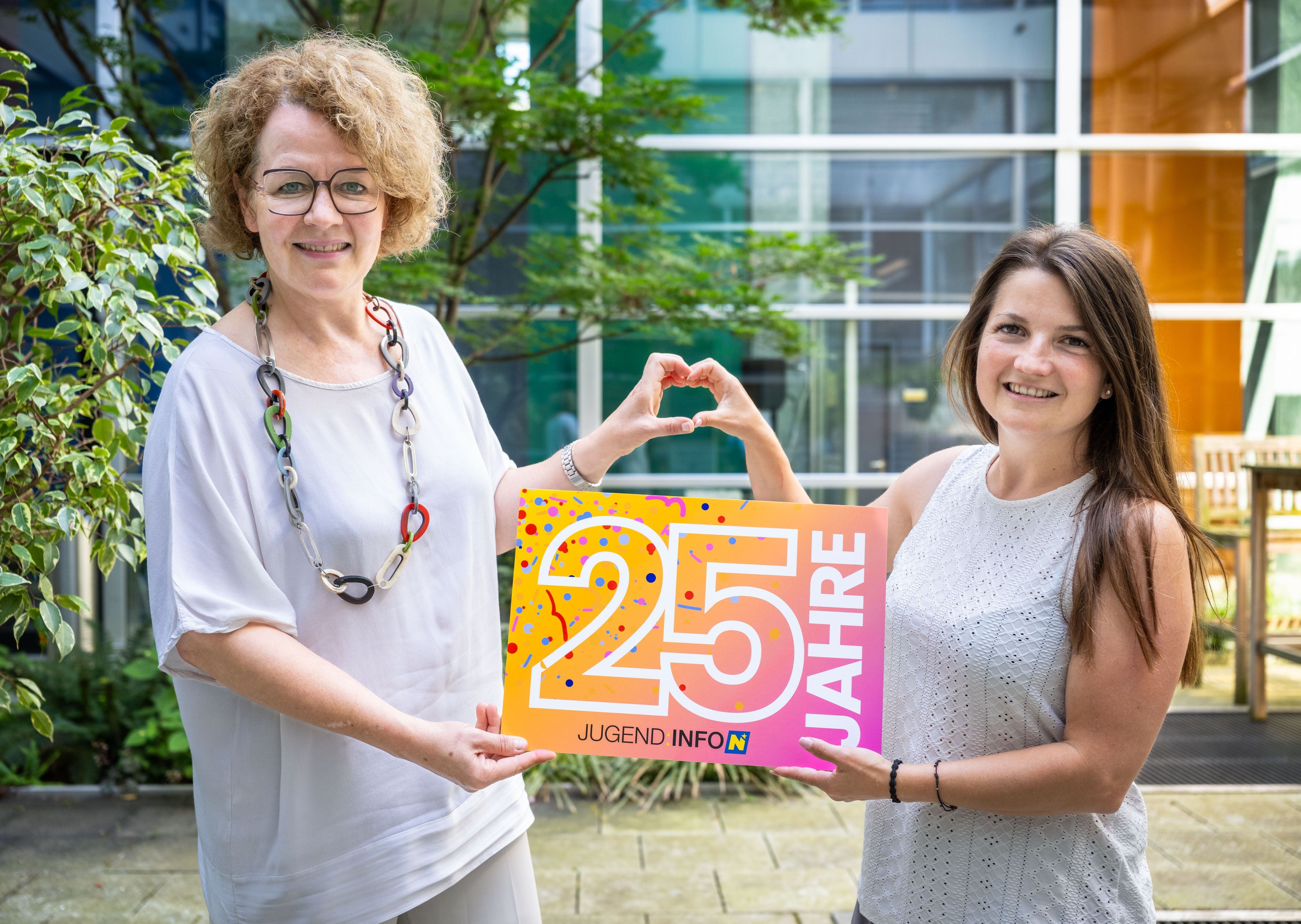 Zwei Frauen halten ein Schild mit „25 Jahre Jugend Info NÖ“ und formen gemeinsam ein Herz mit den Händen.