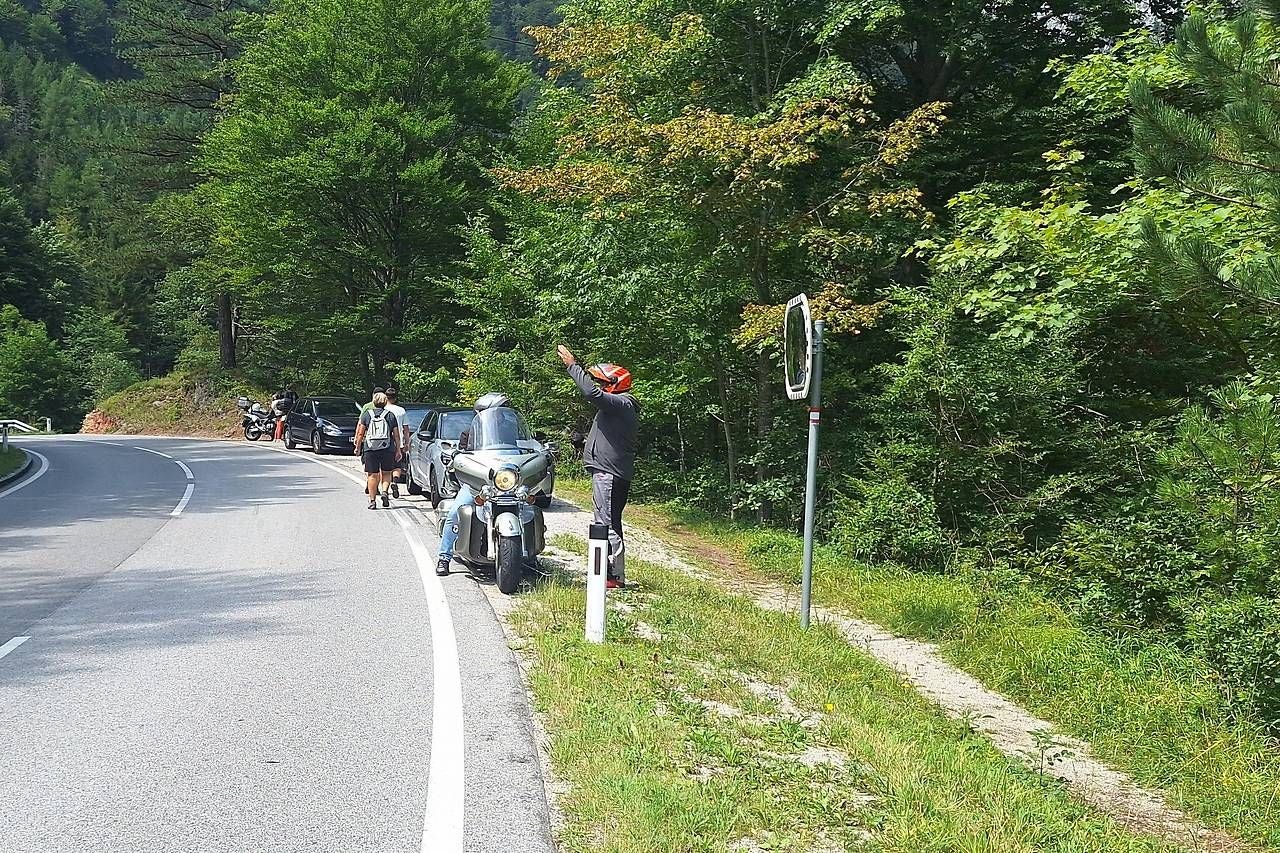 Mehrere Fahrzeuge blockieren den Wanderweg, sodass Wanderer auf die Straße ausweichen müssen.