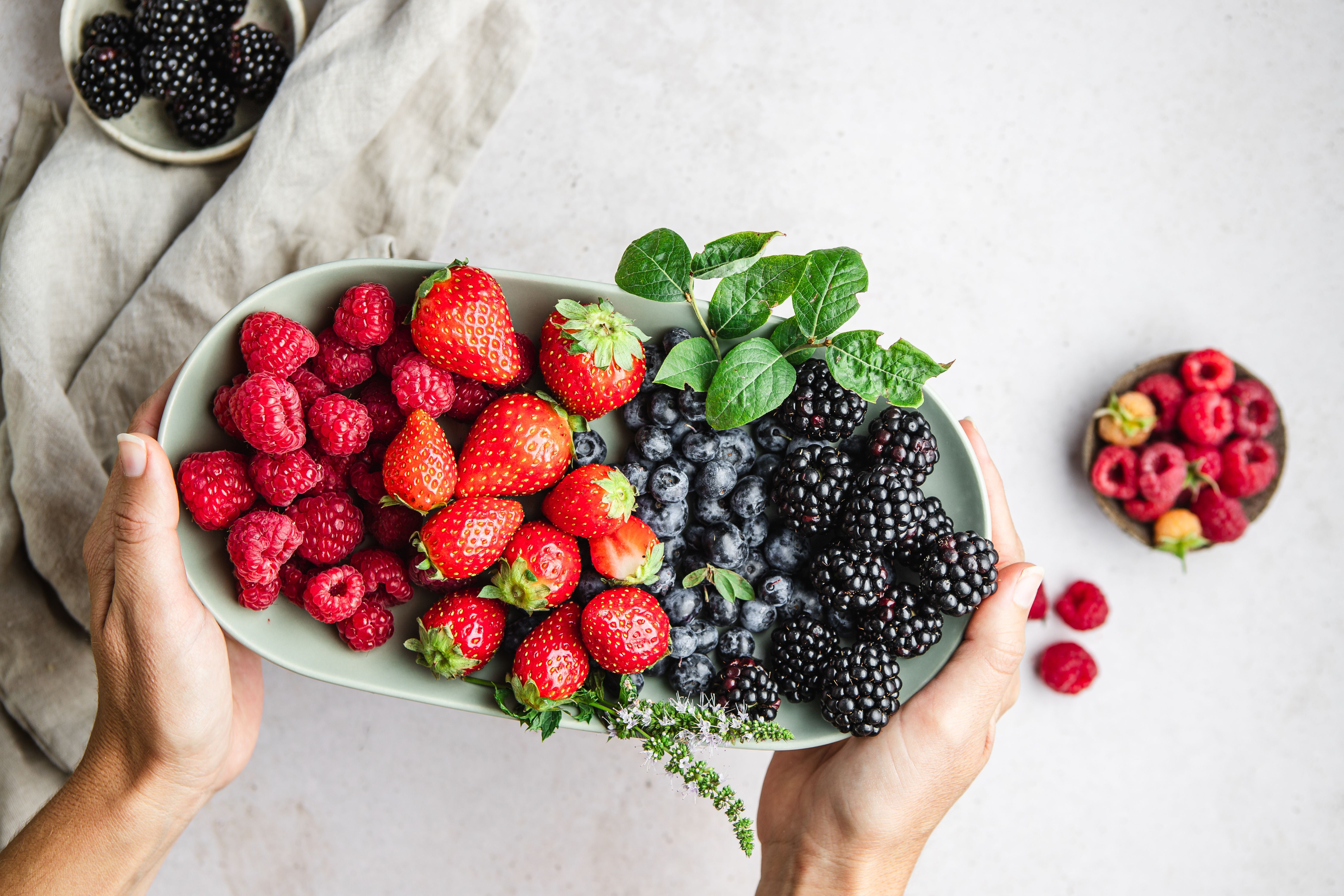Frau hält einen Teller mit frischen Himbeeren, Erdbeeren, Heidelbeeren und Brombeeren.