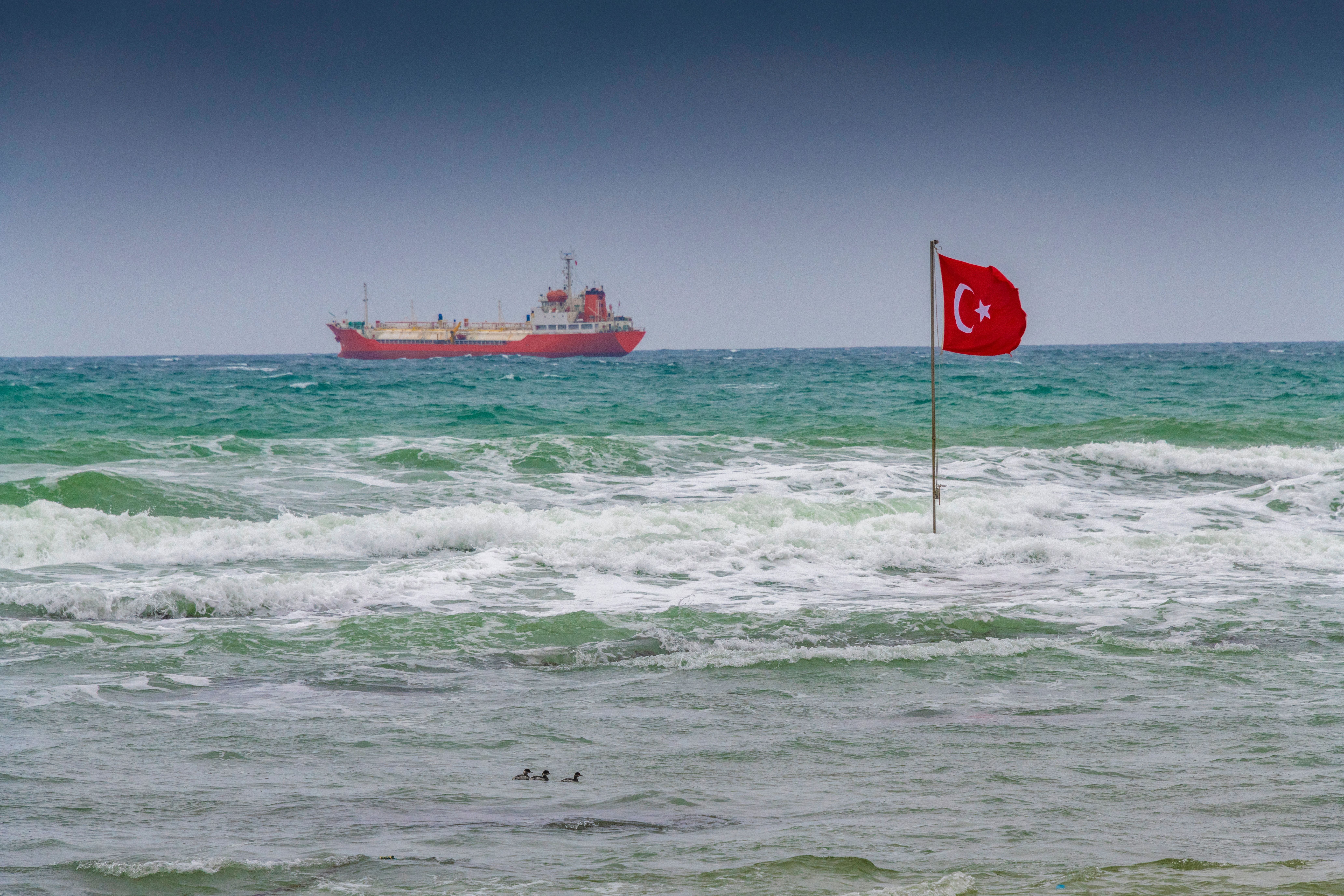 Große Wellen, ein Frachtschiff und eine türkische Fahne am stürmischen Strand von Kisirkaya.