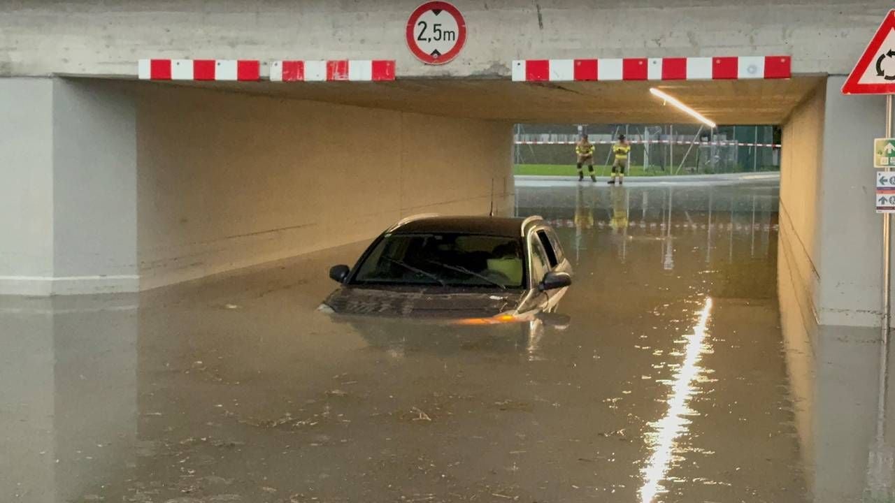 Ein Auto steht halb im Wasser in einer überfluteten Unterführung in Tirol, Feuerwehr im Hintergrund.