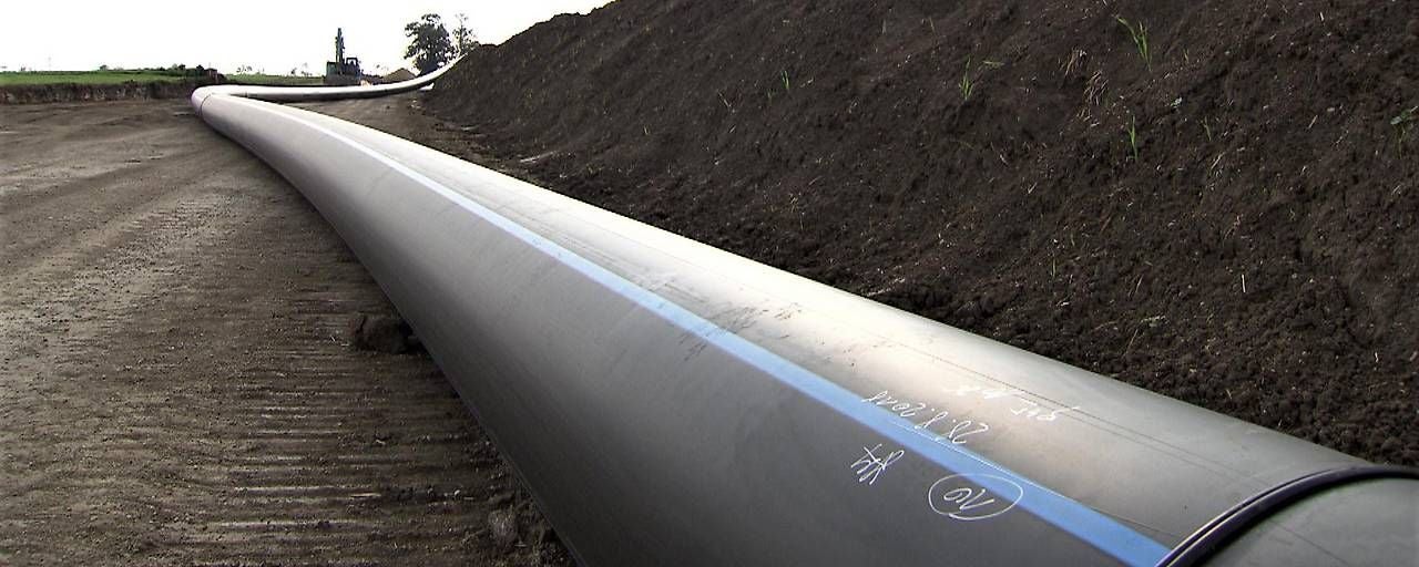 Eine lange, dicke Pipeline liegt neben einem Erdwall auf einer Baustelle im Freien.