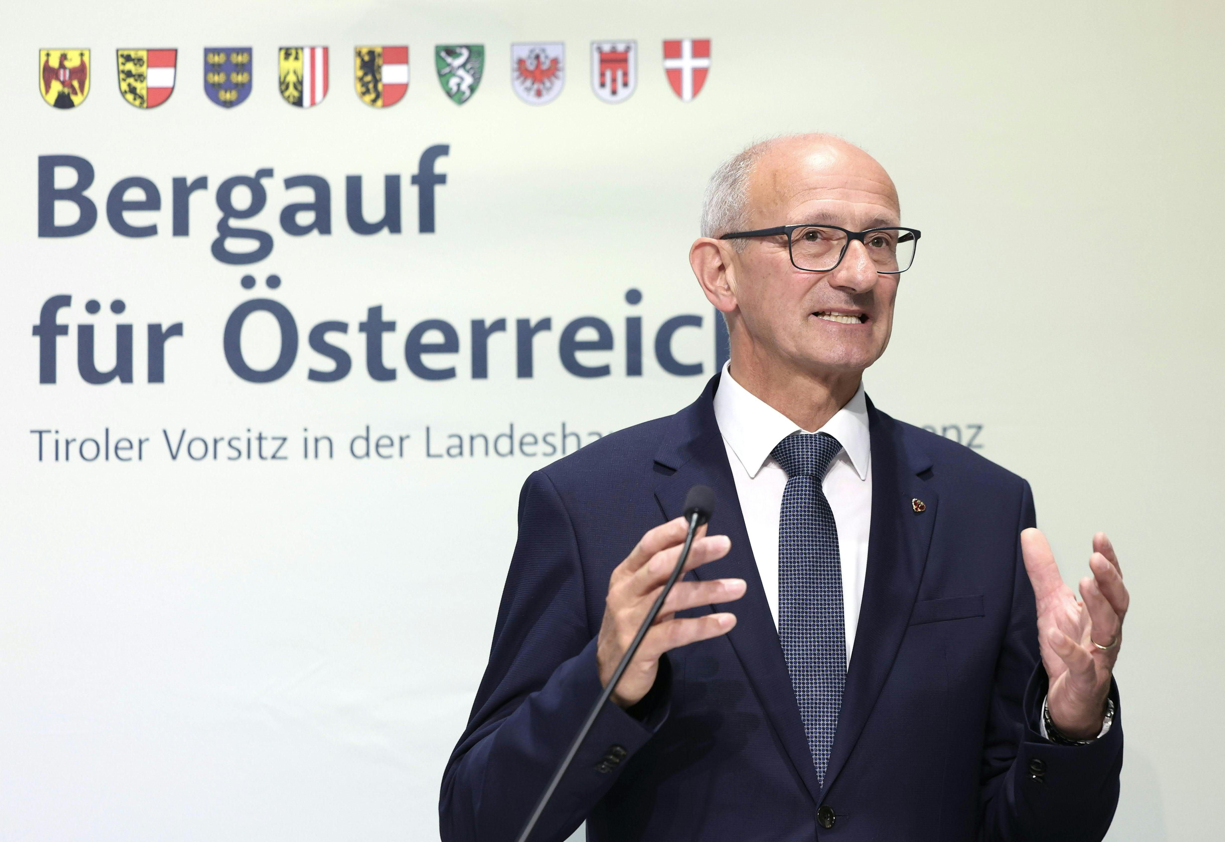 Ein Mann im Anzug spricht bei einer Pressekonferenz vor einem Schild mit „Bergauf für Österreich“.