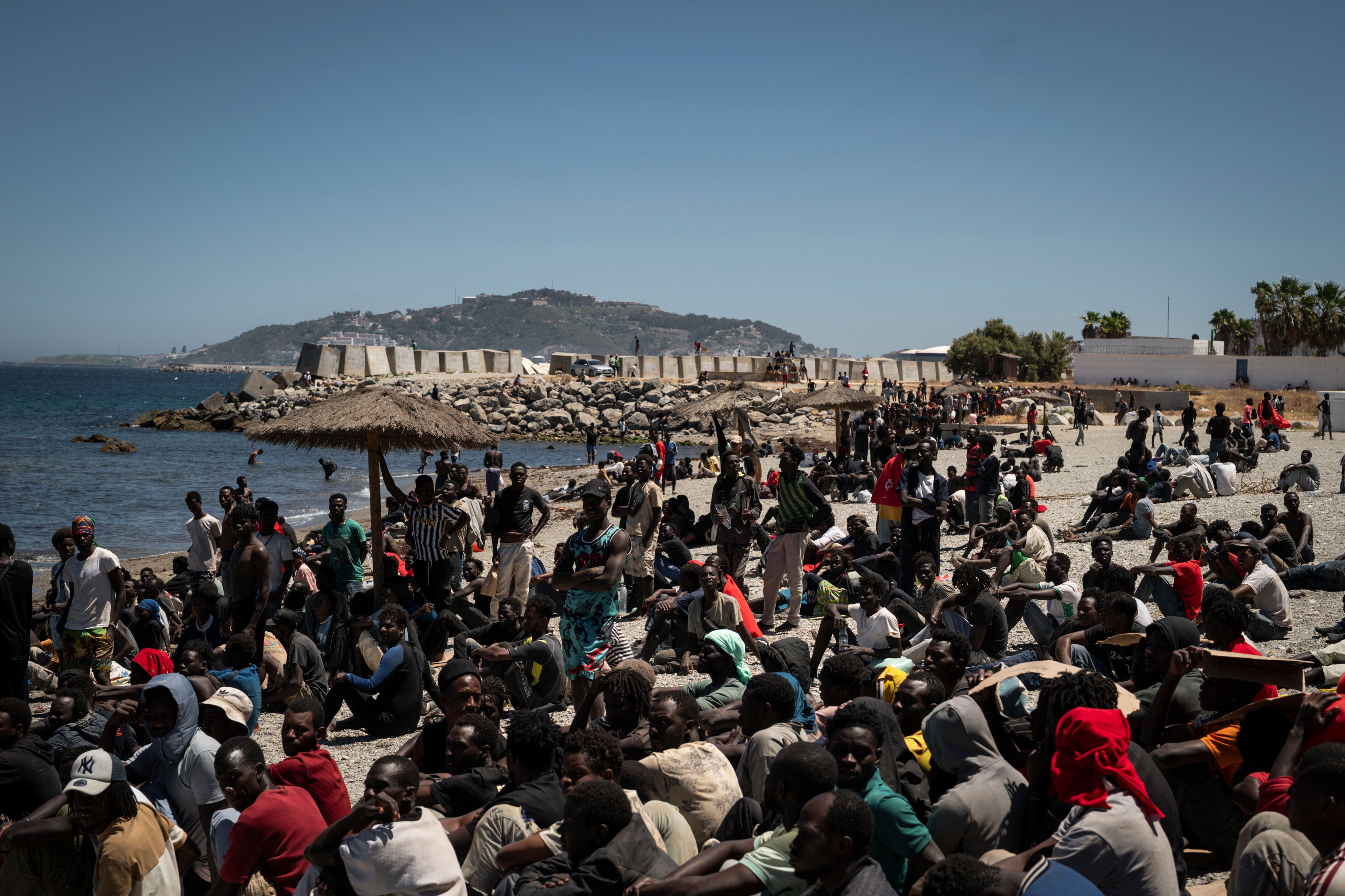 Viele Menschen sitzen und stehen dicht gedrängt an einem Strand nahe dem Wasser in Ceuta, Spanien.