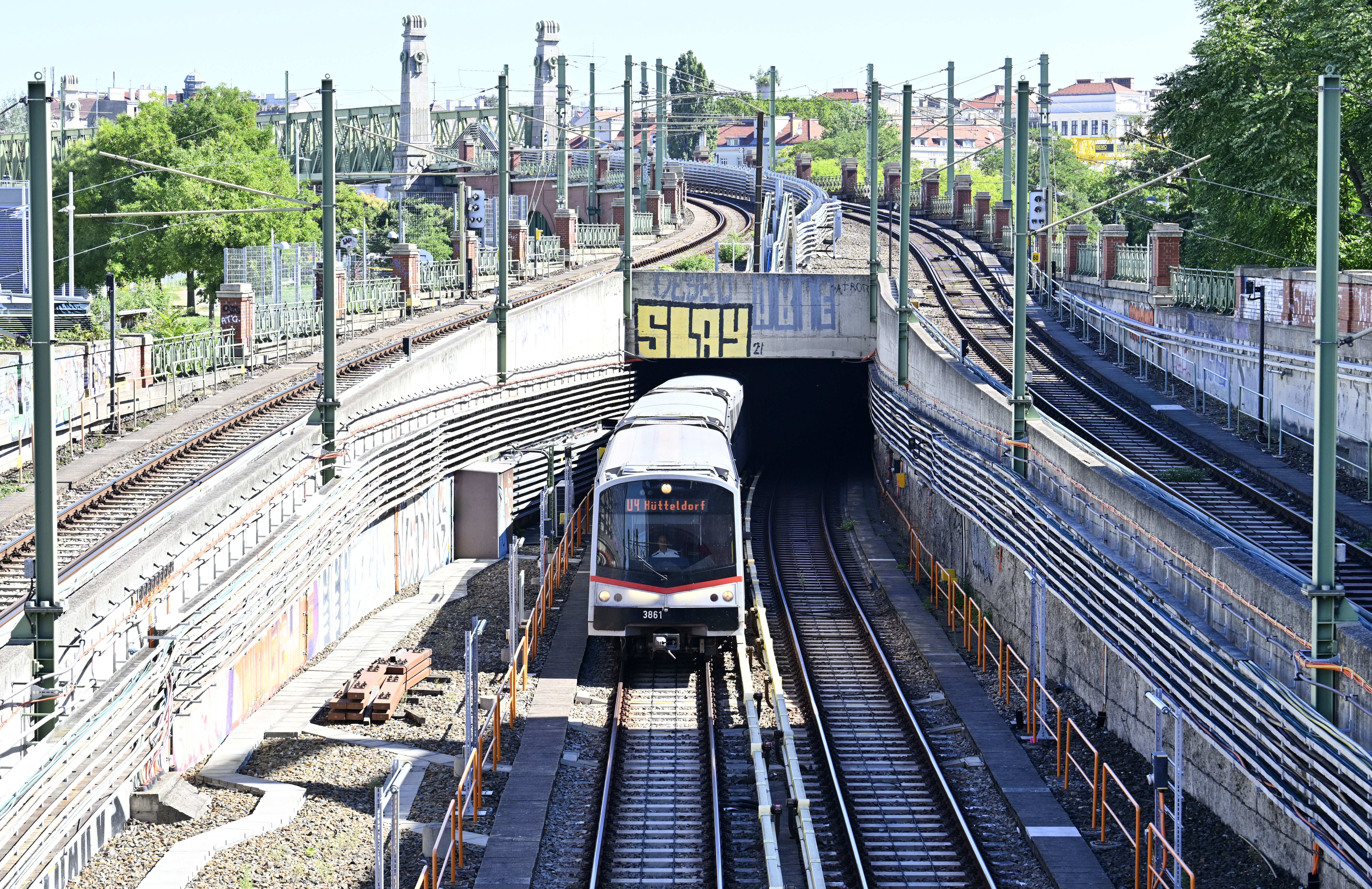 Eine U-Bahn der Linie U4 fährt aus einem Tunnel in Wien bei sonnigem Wetter heraus.
